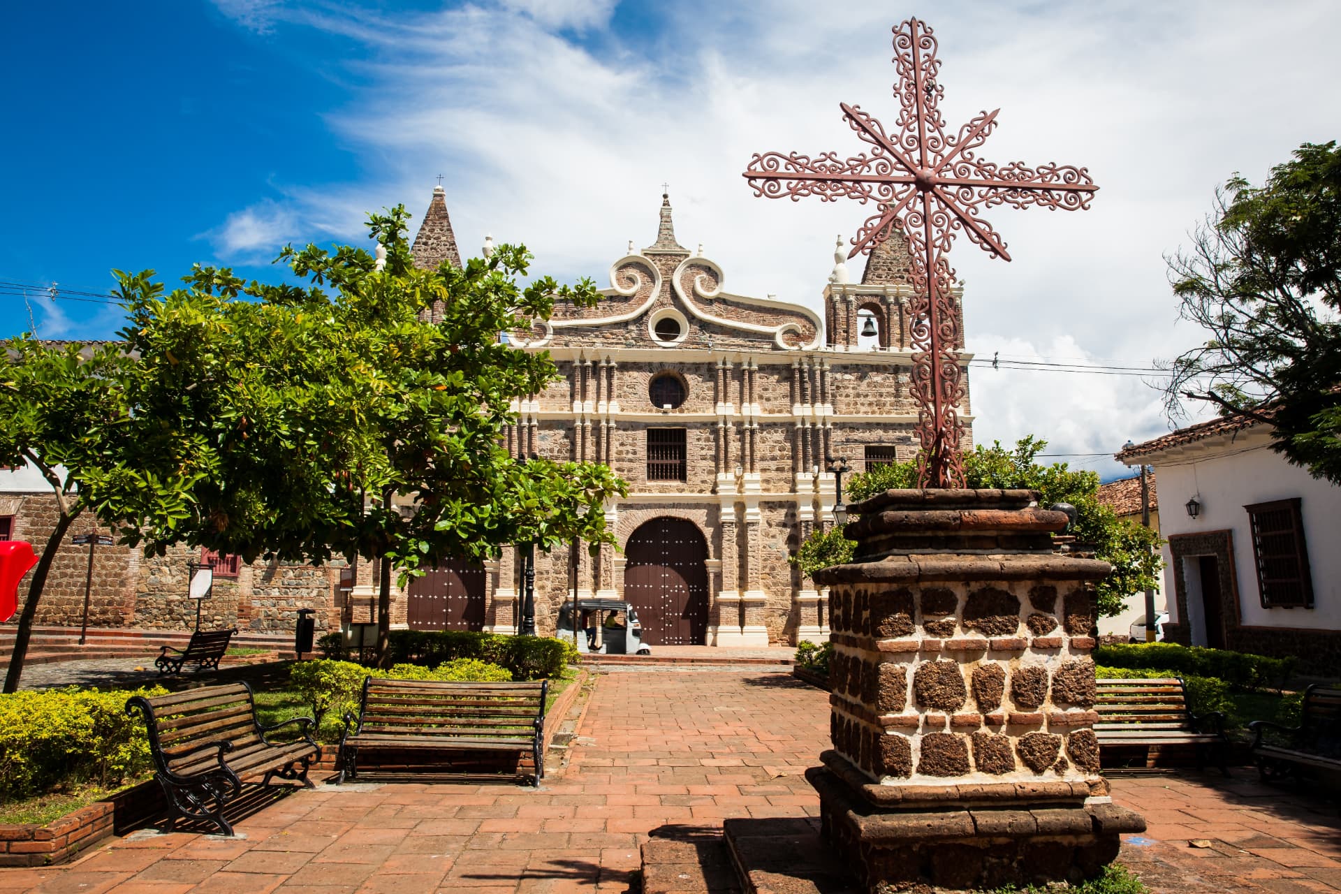 Historic church and ornate iron cross in a leafy square in Santa Fe de Antioquia