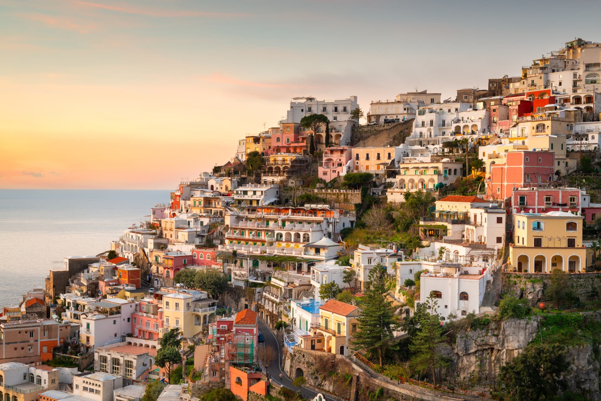 Positano's pastel houses stacked down the cliffside to the sea at sunset