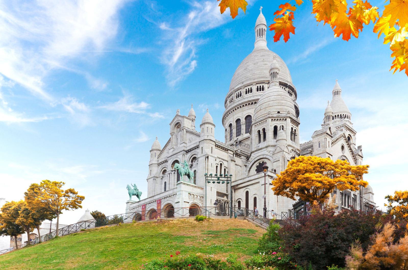 Sacré-Cœur Basilica on Montmartre hill framed by golden autumn leaves and a bright blue sky