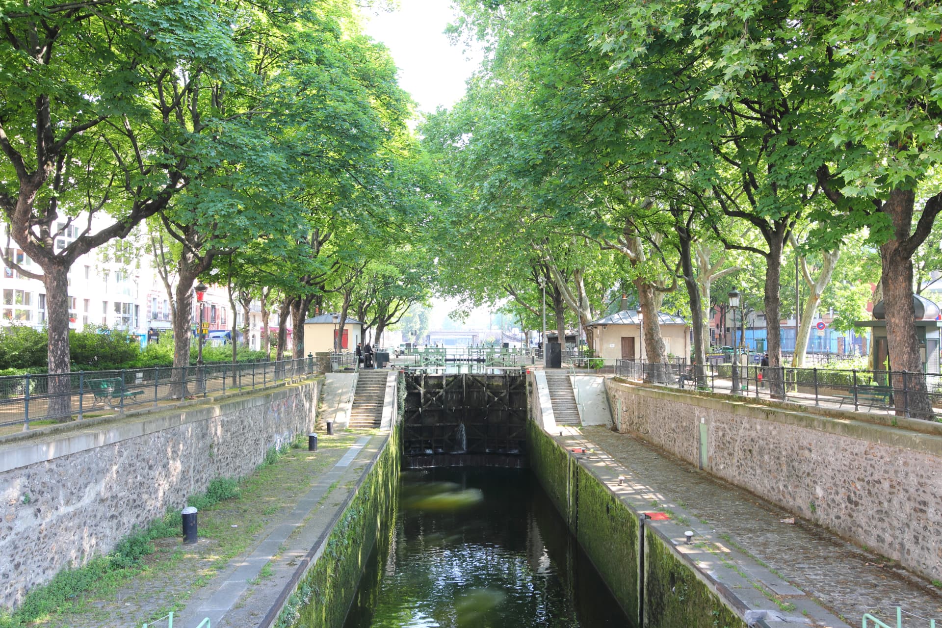 The Canal Saint-Martin drawn down inside its lock chamber, with stone walls, green gates and plane trees above