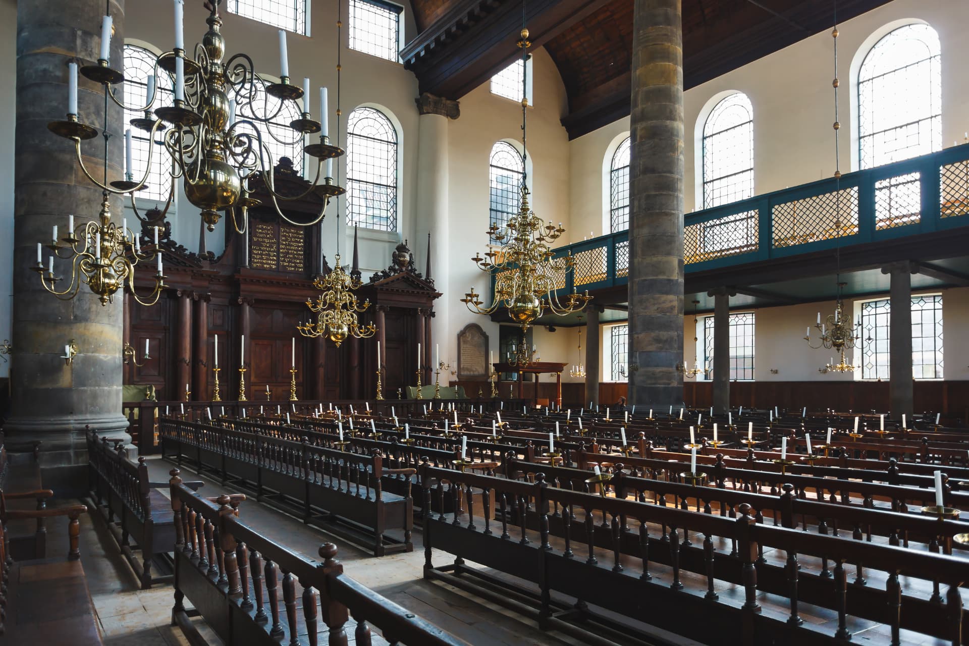 The interior of the Portuguese Synagogue in Amsterdam with brass chandeliers, dark wooden benches, tall columns and arched windows