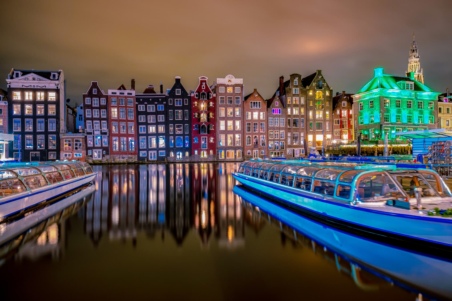 Gabled canal houses and tour boats reflected in an Amsterdam canal at night