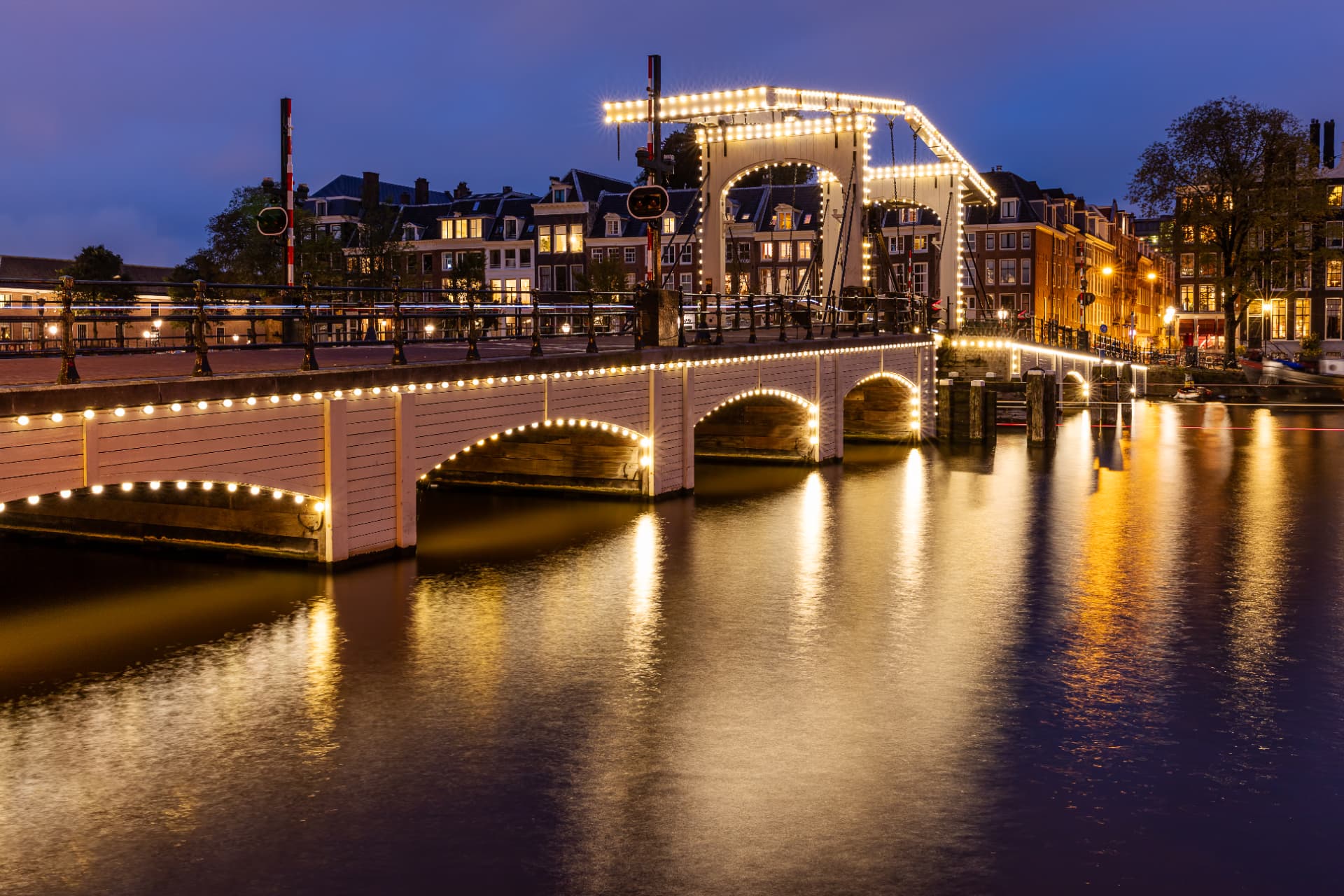 The Magere Brug in Amsterdam illuminated by strings of lights at dusk, reflected in the river Amstel