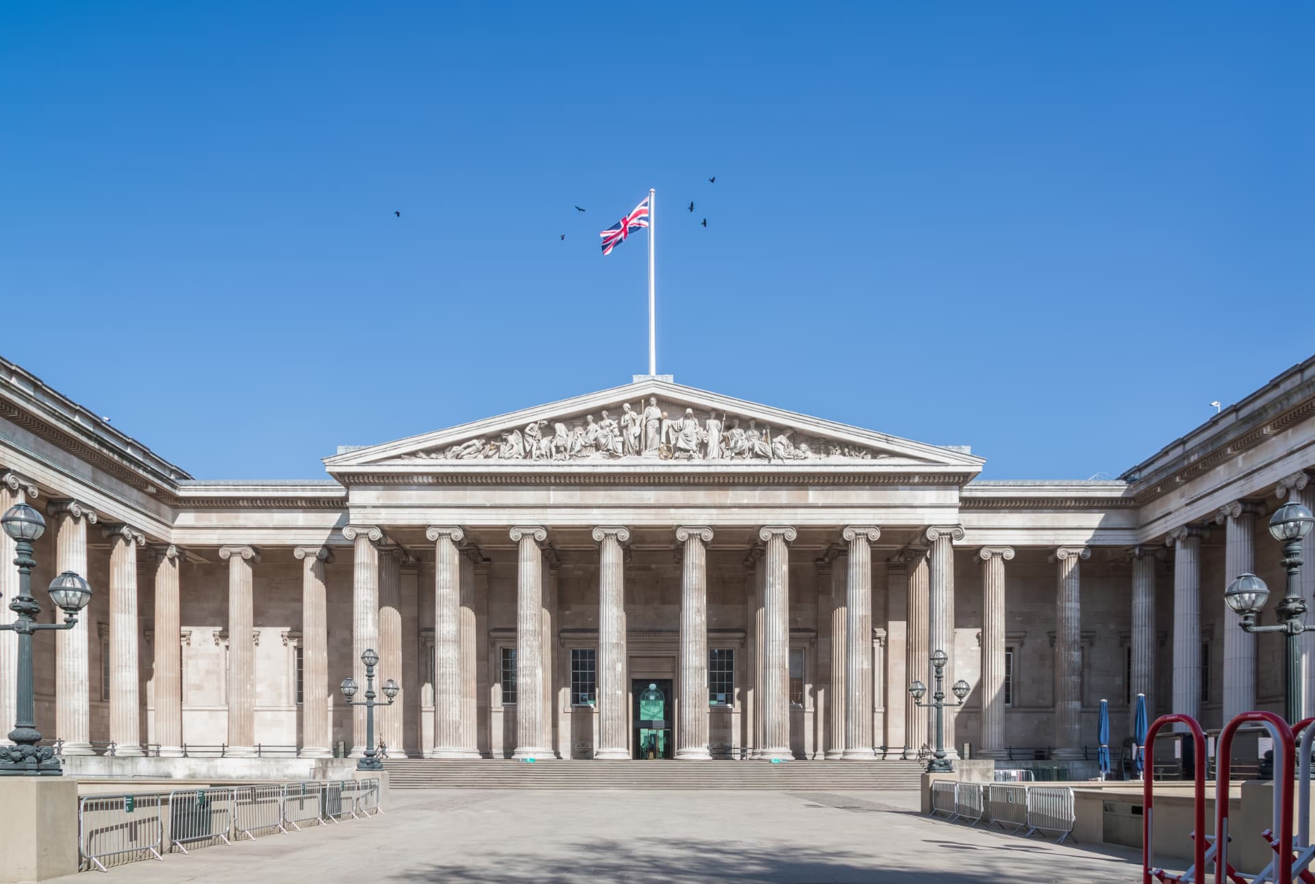 The British Museum exterior with its columns, pediment and Union Jack flag under a blue sky