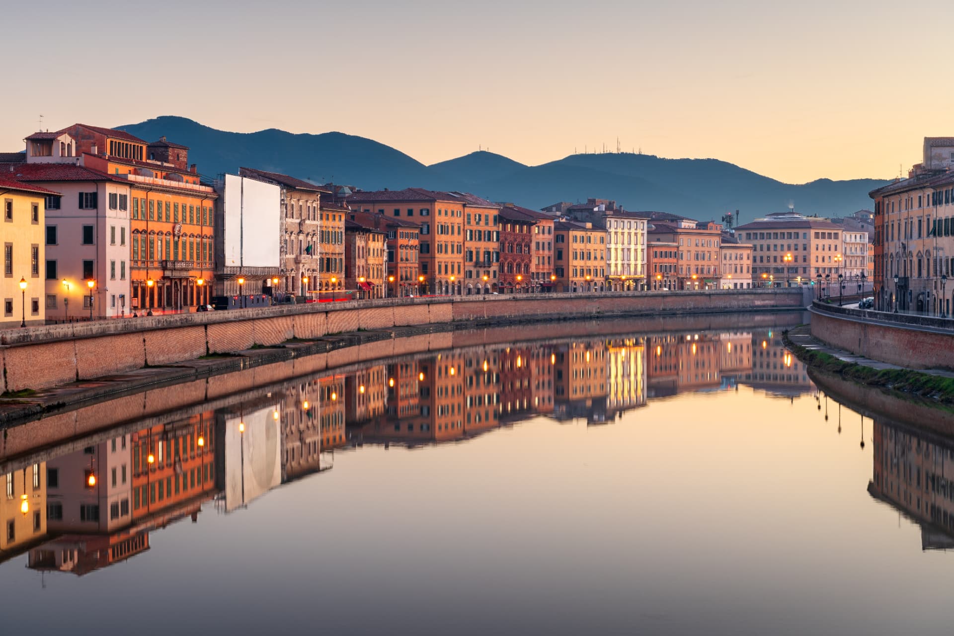 Colourful buildings along the River Arno in Pisa reflected in the water at dusk