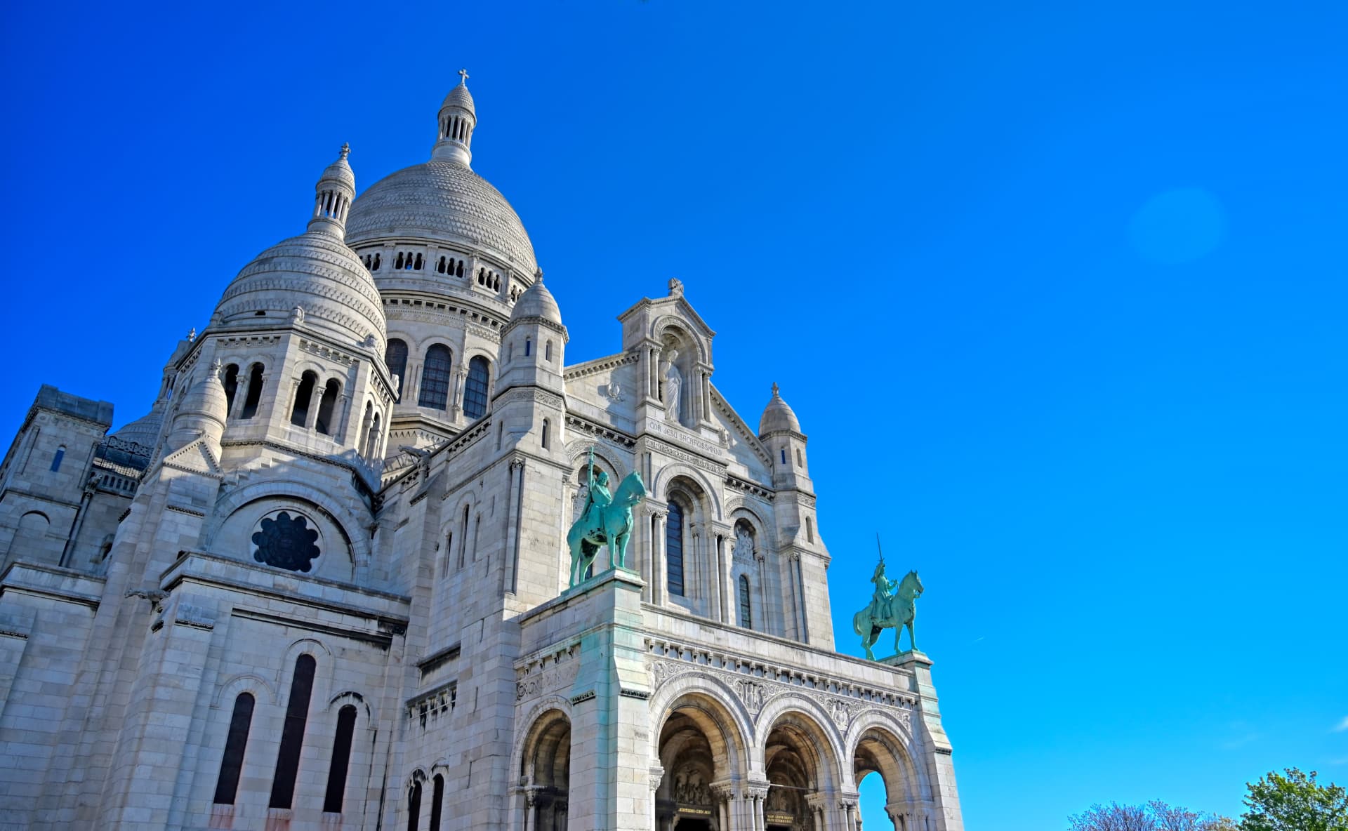 Low-angle view of the white domes and entrance porch of Sacré-Cœur against a bright blue sky