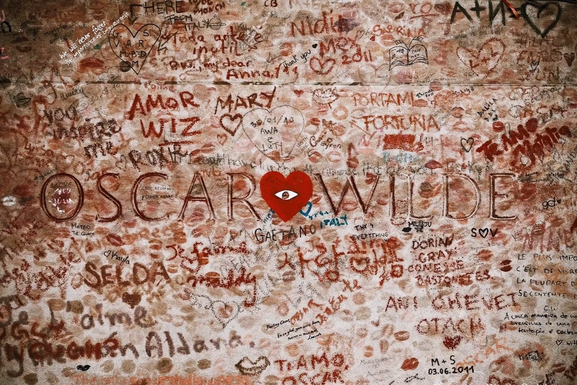 The glass barrier at Oscar Wilde's tomb in Père Lachaise, covered in handwritten messages and a red heart