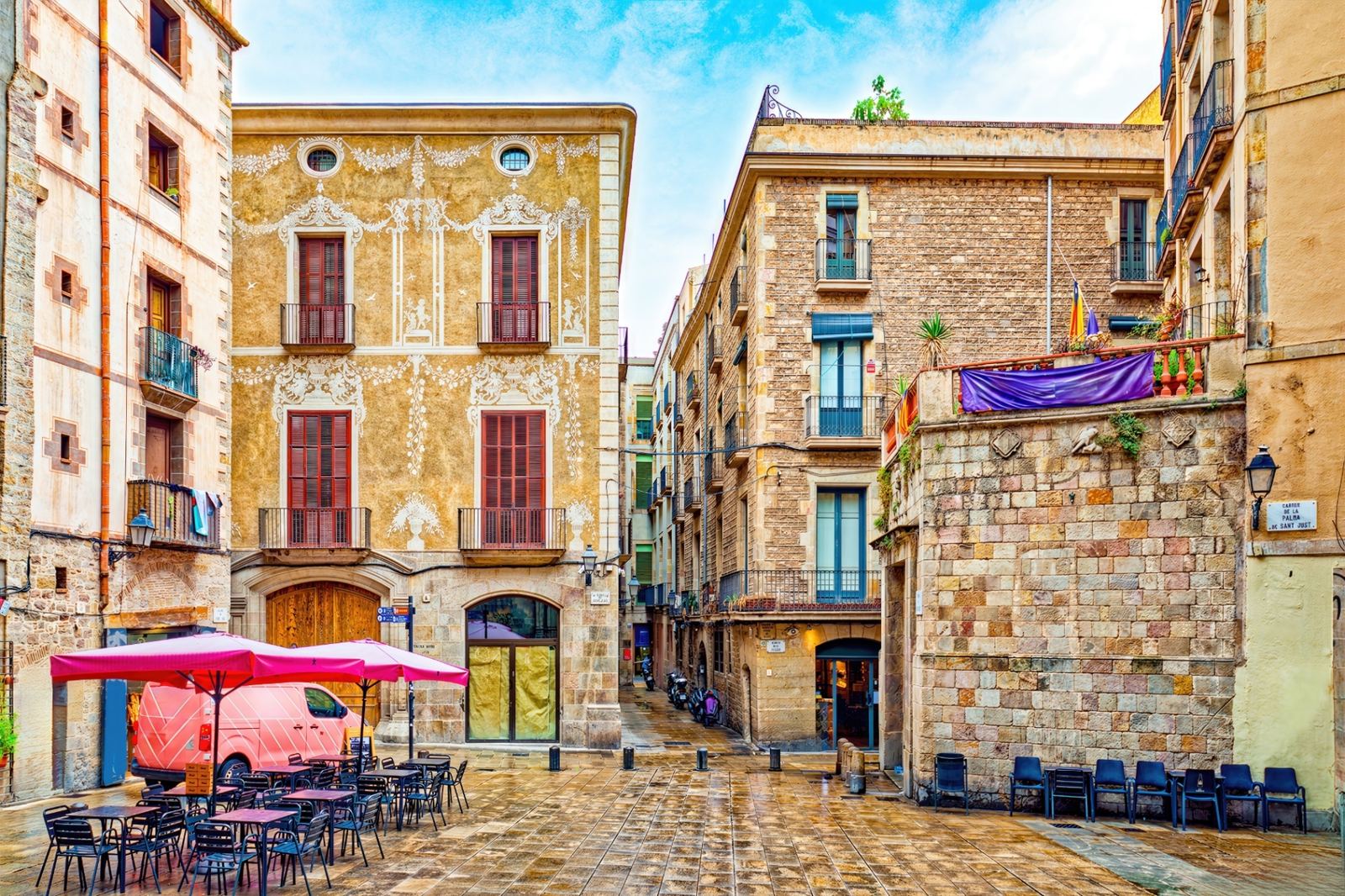 Colorful Gothic Quarter square with historic painted facades, outdoor café tables and medieval stone buildings in Barcelona