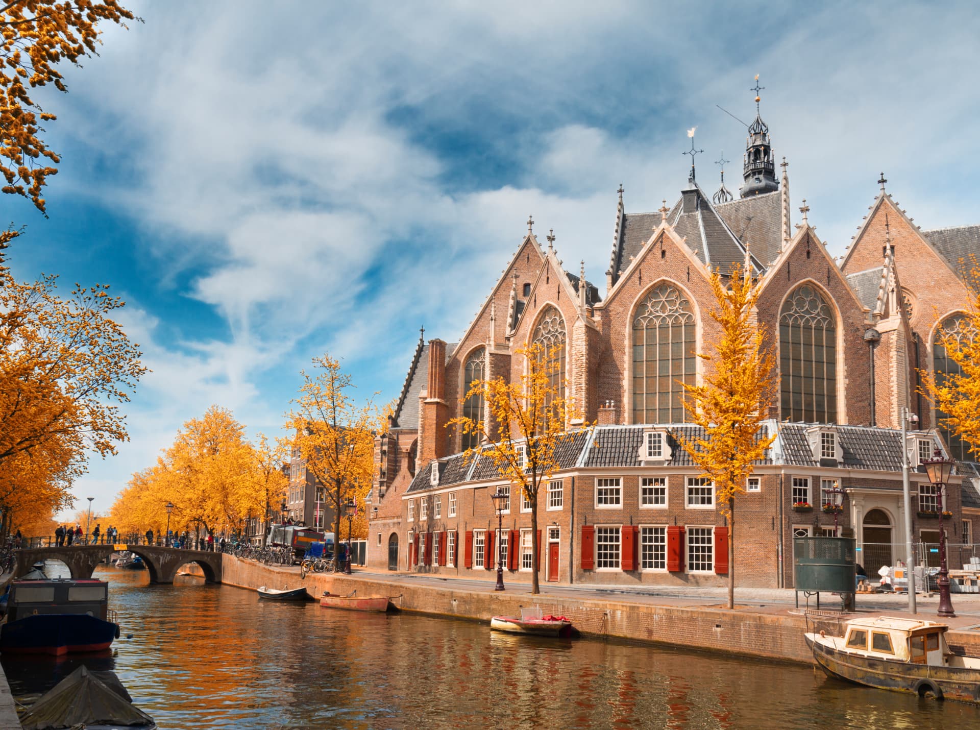 Gothic gables and tall windows of the Oude Kerk beside a canal lined with golden autumn trees