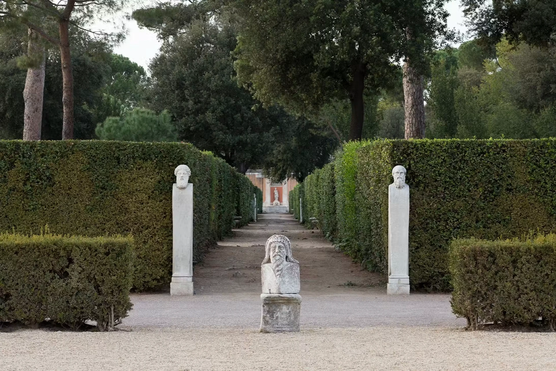 Gravel garden avenue lined with clipped hedges and carved herm busts at Villa Medici
