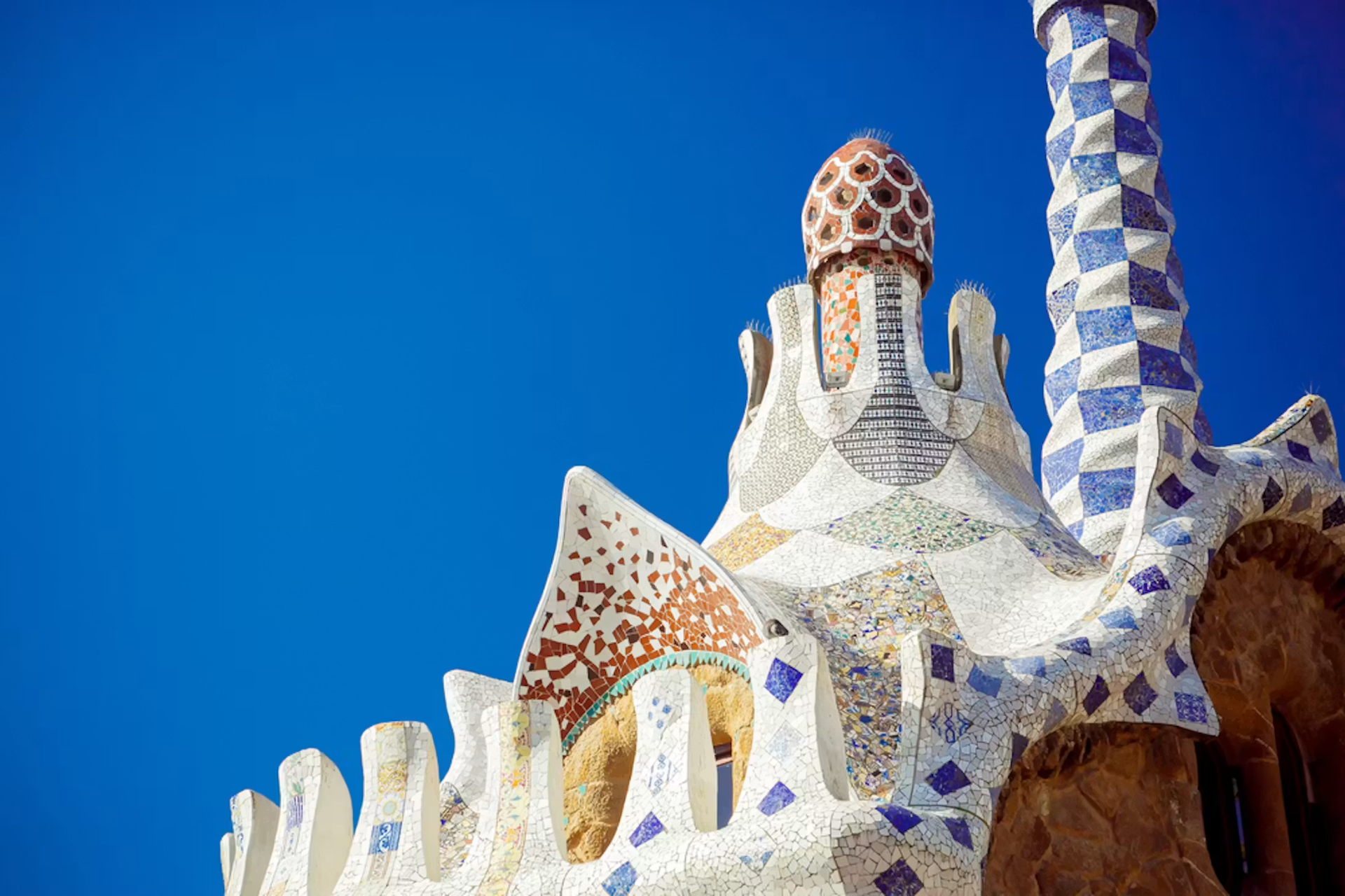 Colorful Park Güell mosaic tower and tiled spires against a bright blue Barcelona sky