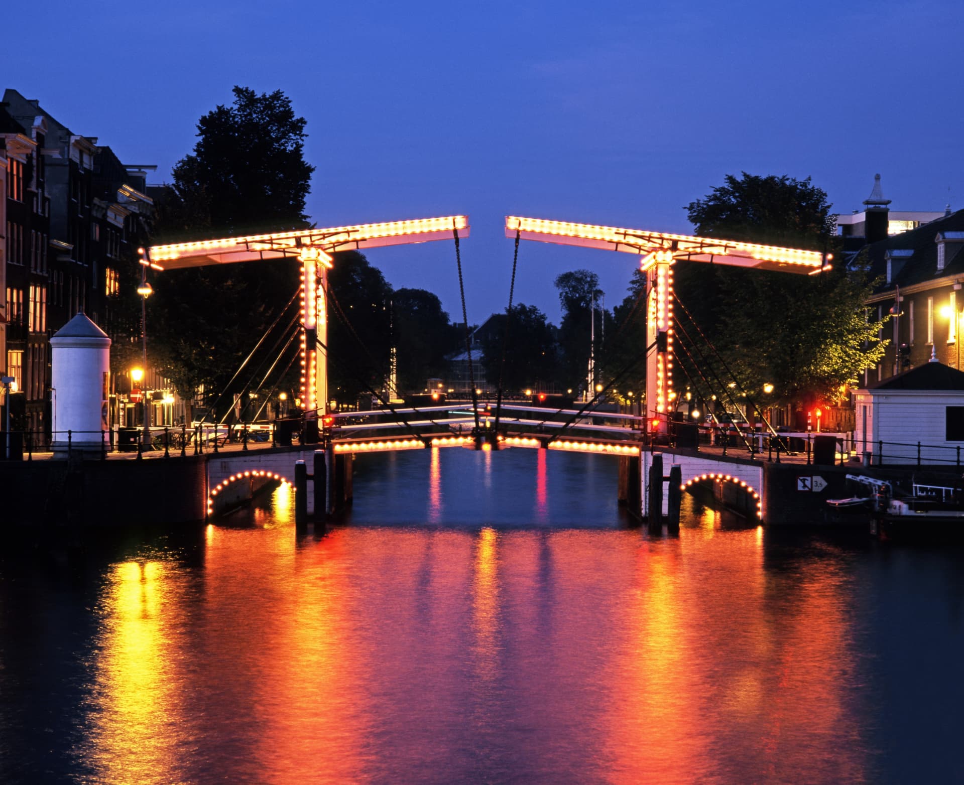The Magere Brug seen head-on from the Amstel at night, its twin illuminated drawbridge leaves reflected in the water