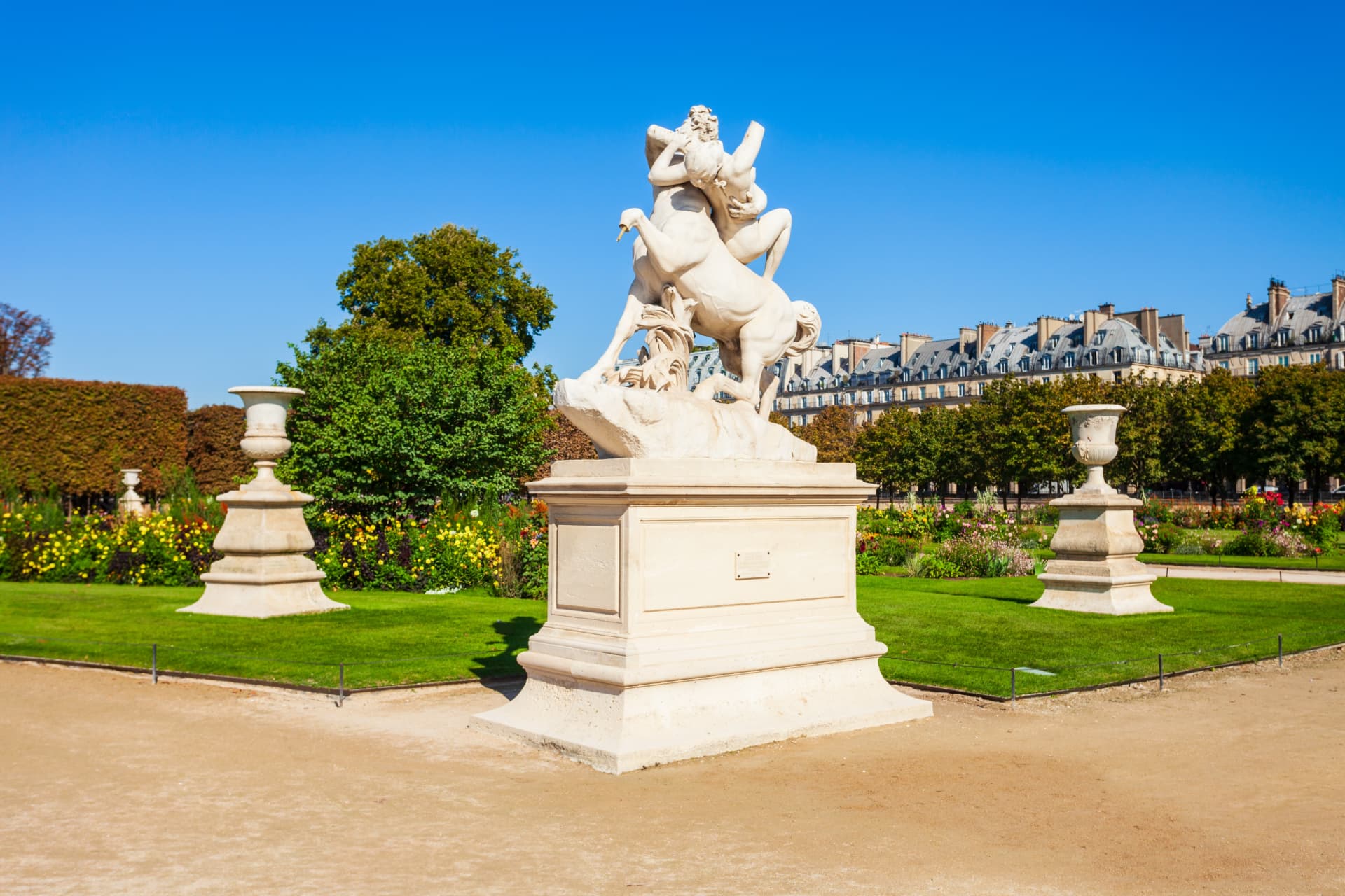 White marble horse sculpture on a plinth among lawns and flower beds in the Tuileries Garden
