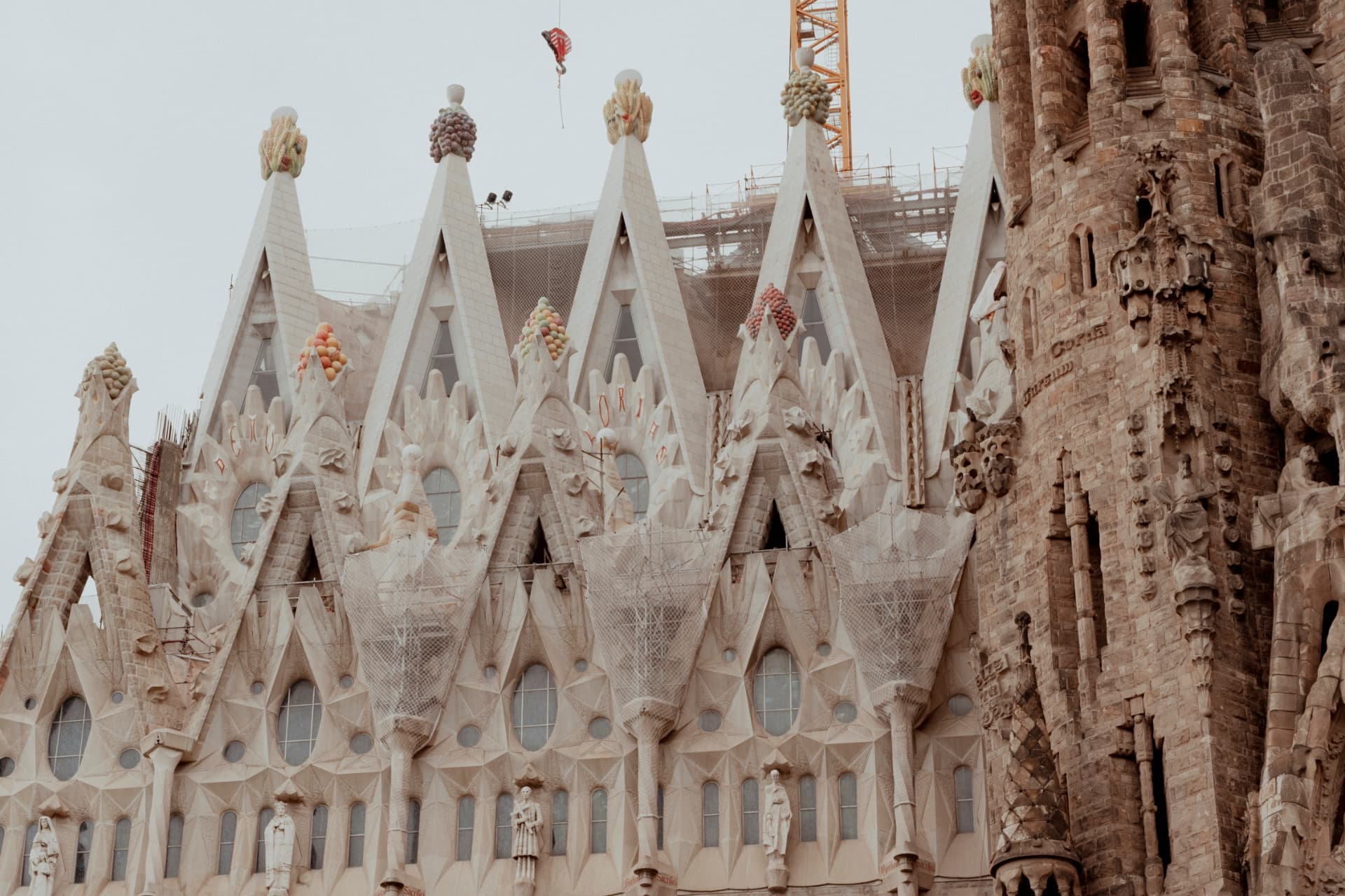 Detailed view of the Sagrada Família's fruit-topped pinnacles and sculpted white spires with construction cranes behind