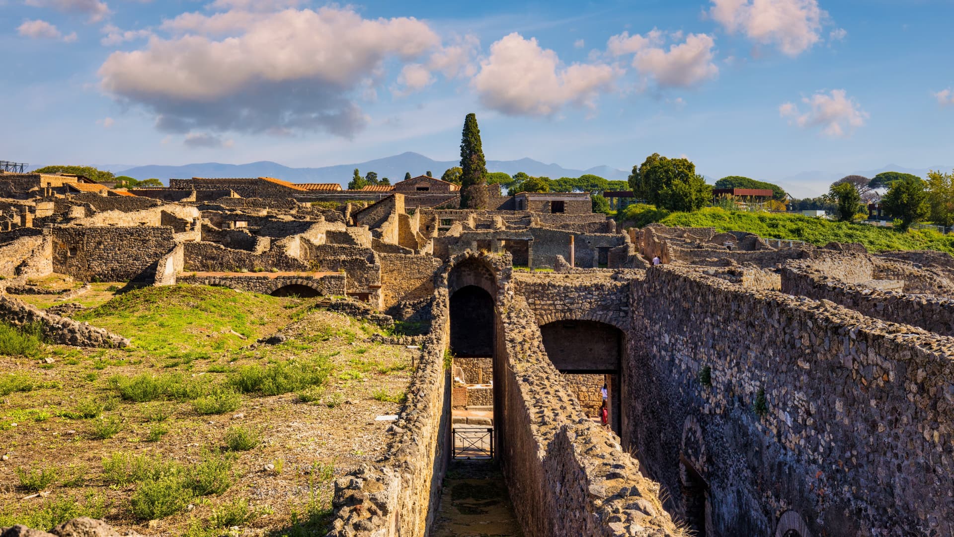 Stone arches and ruined walls inside the Pompeii archaeological park with mountains in the distance