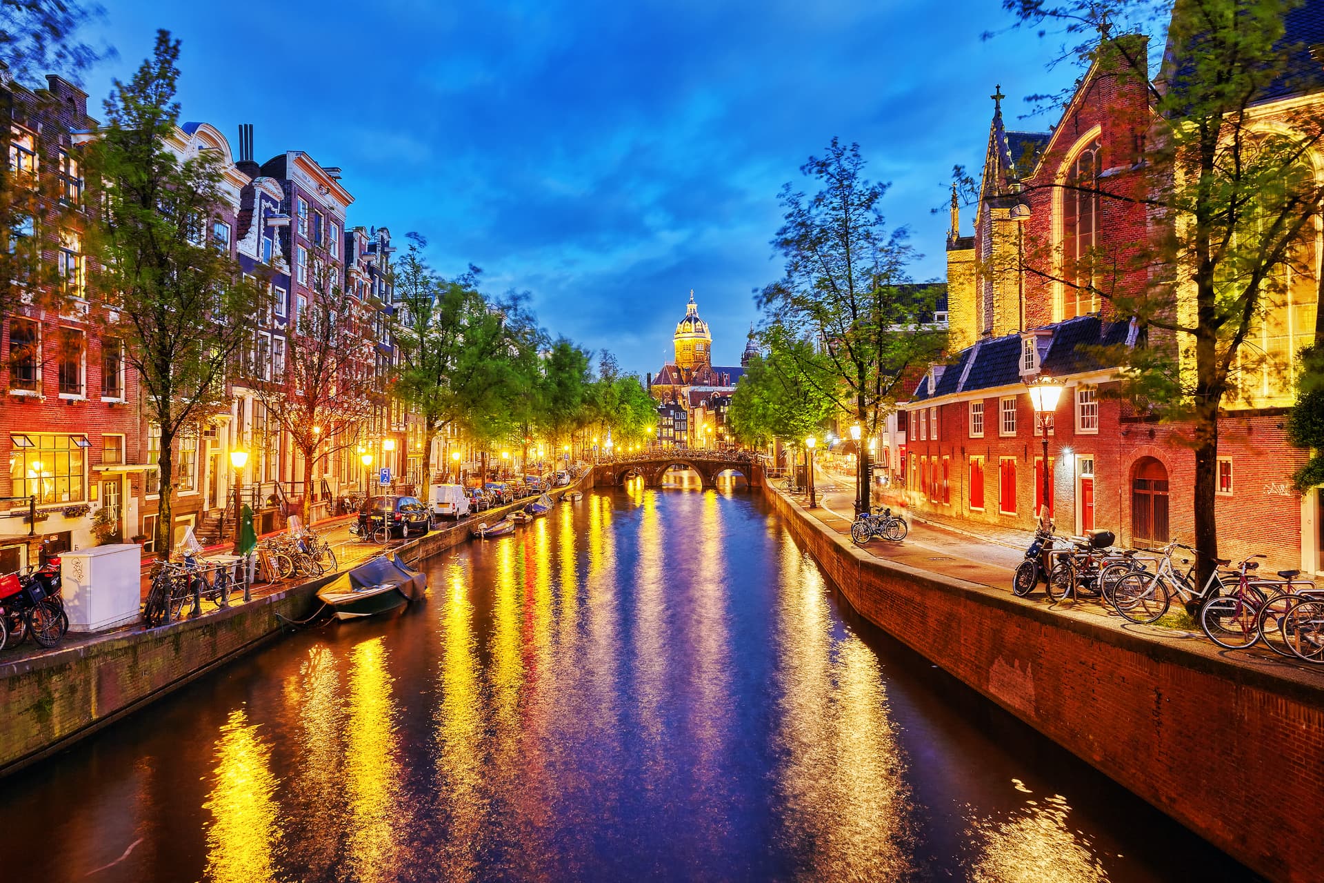 A canal in the Jordaan district of Amsterdam at dusk with bridge lights reflecting in the water