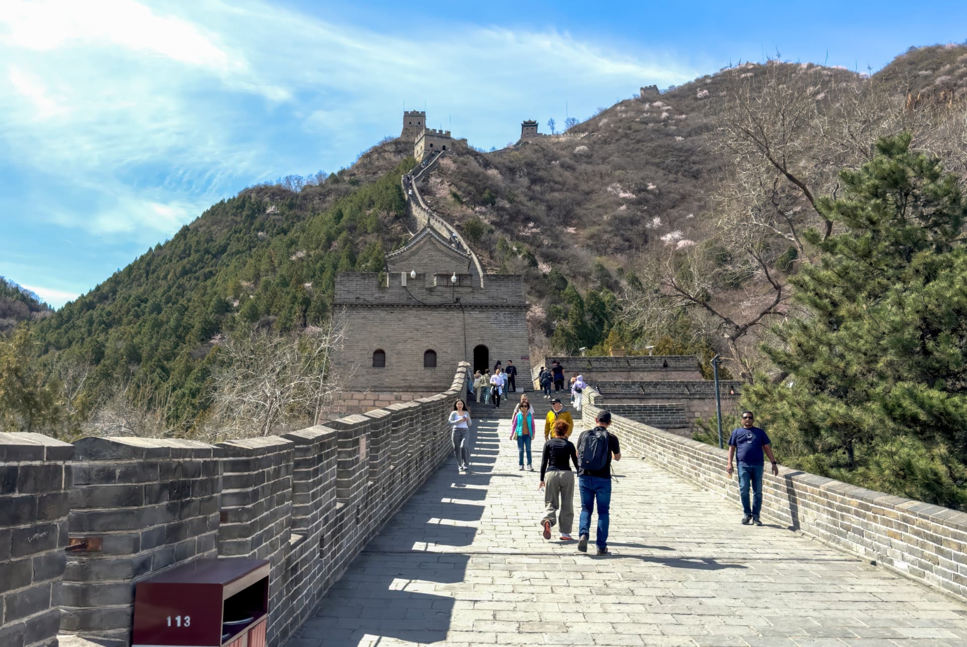 Visitors walking up a broad restored section of the Great Wall towards a watchtower on a wooded hillside