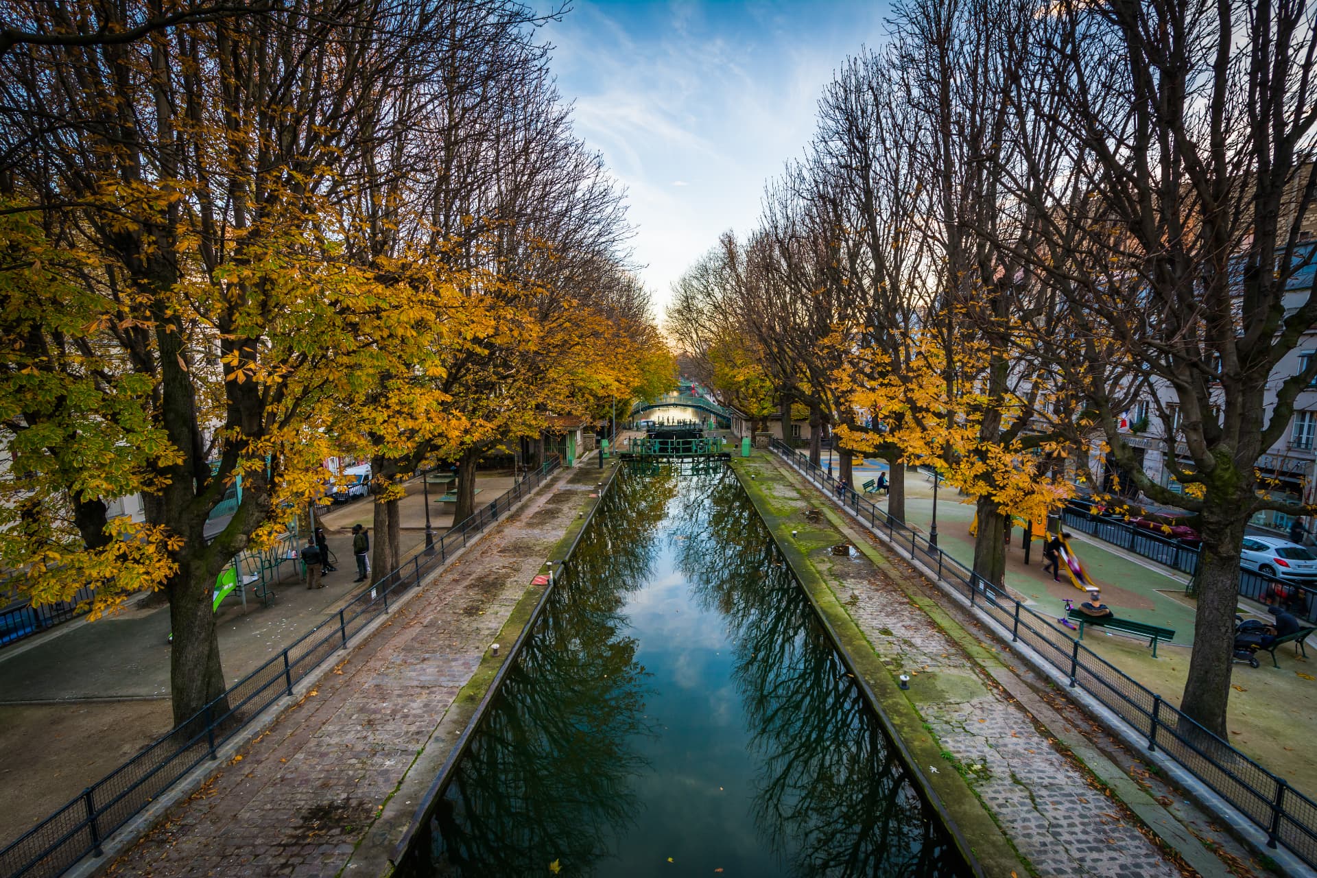 Elevated autumn view along the Canal Saint-Martin in Paris, with yellow plane trees lining both quays and a lock gate in the centre