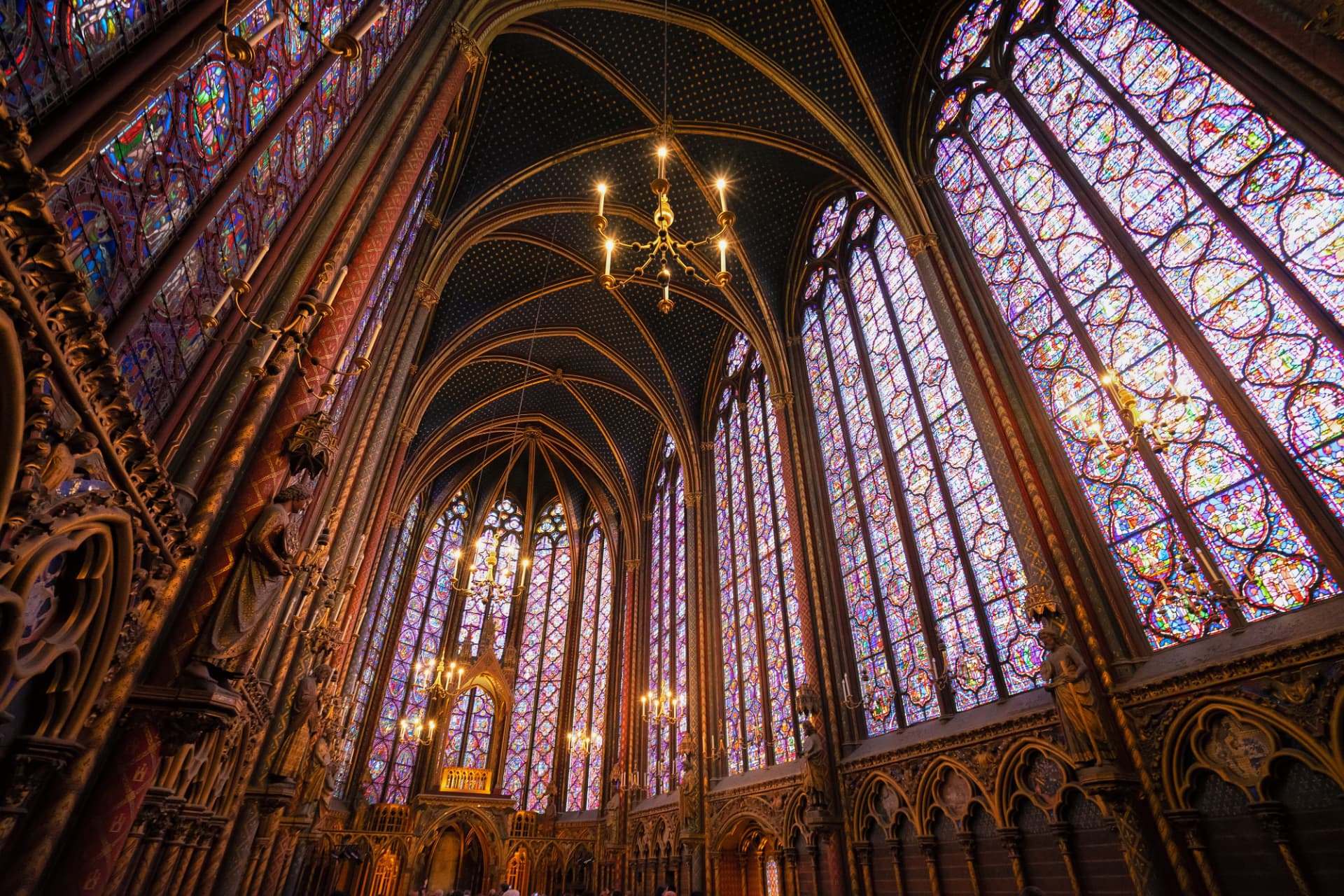 Stained-glass windows of Sainte-Chapelle's upper chapel glowing in daylight with a gilded chandelier