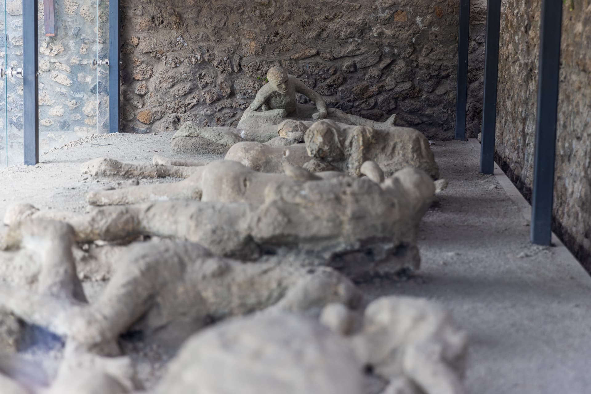 Plaster casts of Pompeii eruption victims displayed behind glass in a stone-walled shelter