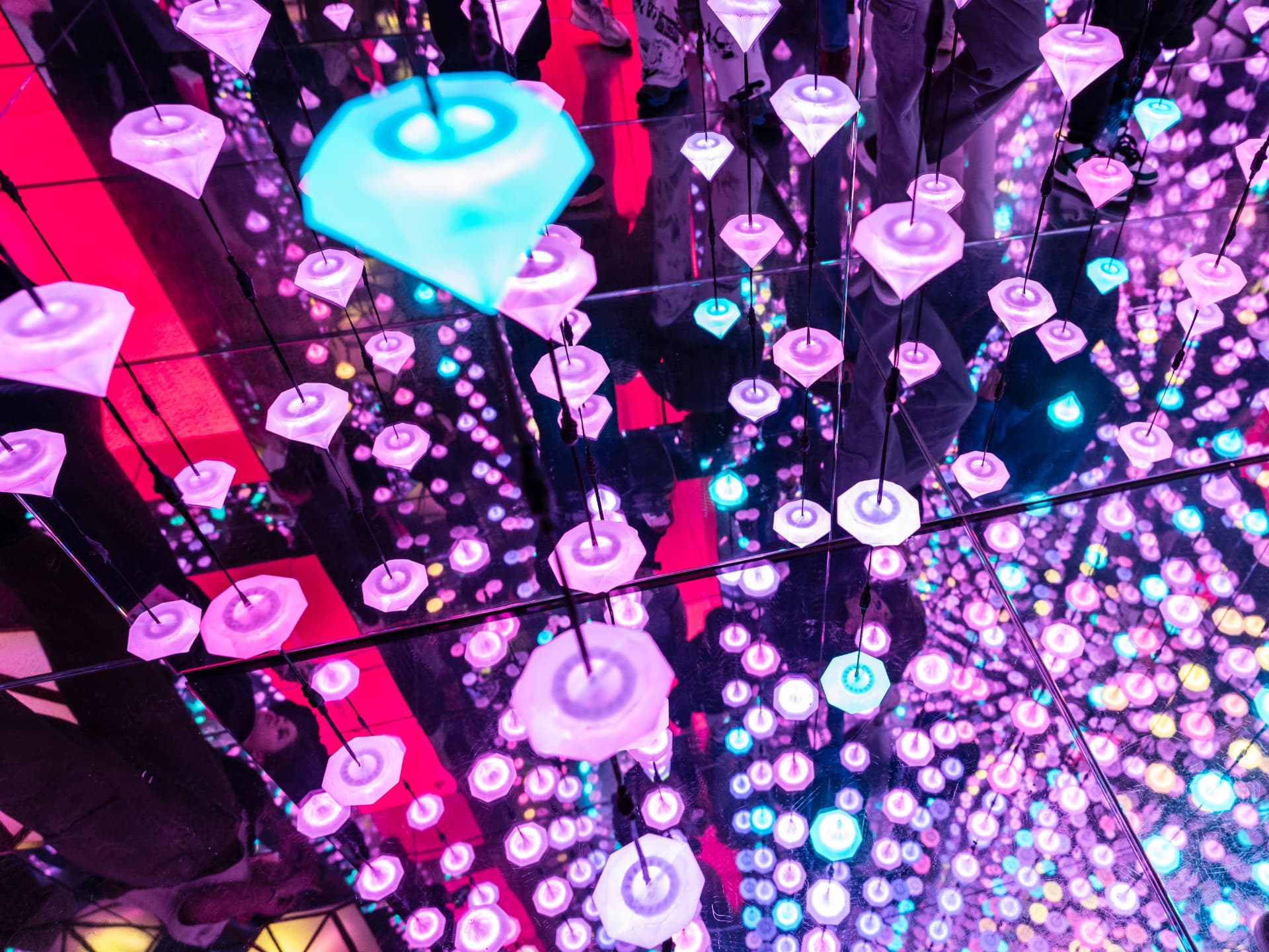 A mirrored immersive room at the Moco Museum filled with hanging glowing pink and turquoise diamond-shaped lights