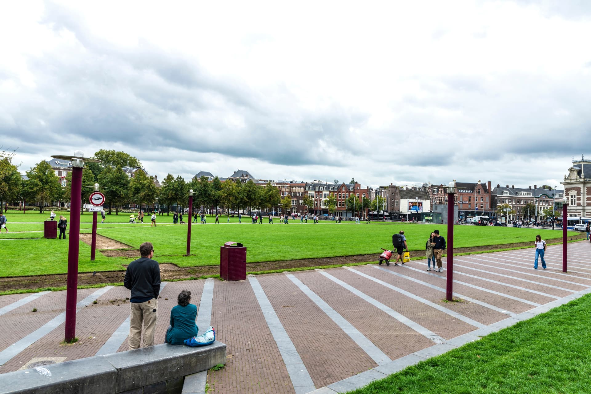 Visitors walking along the brick paths beside the Museumplein lawn on a cloudy day