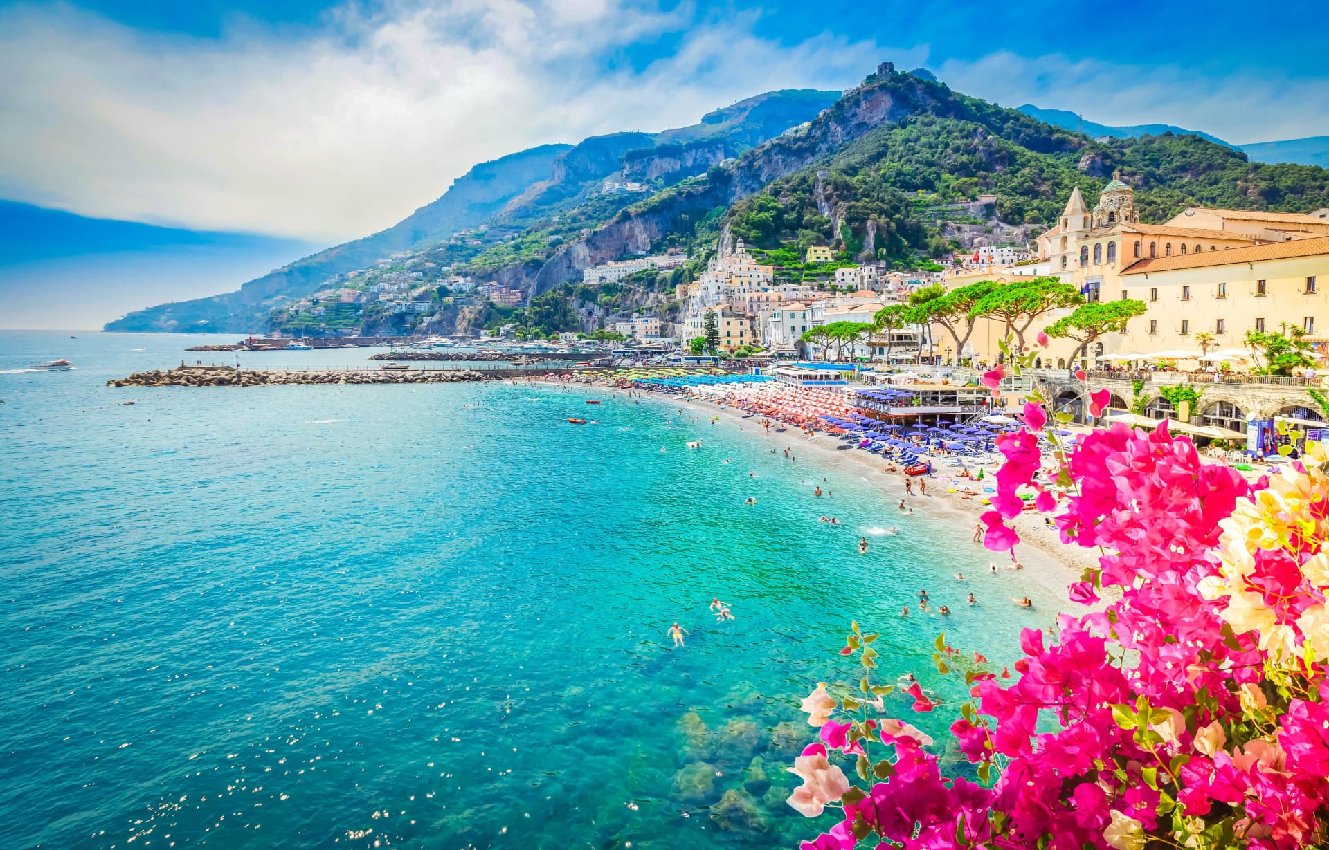 Amalfi town beach and harbour seen from the coastal road, with the cathedral bell tower and cliffs behind