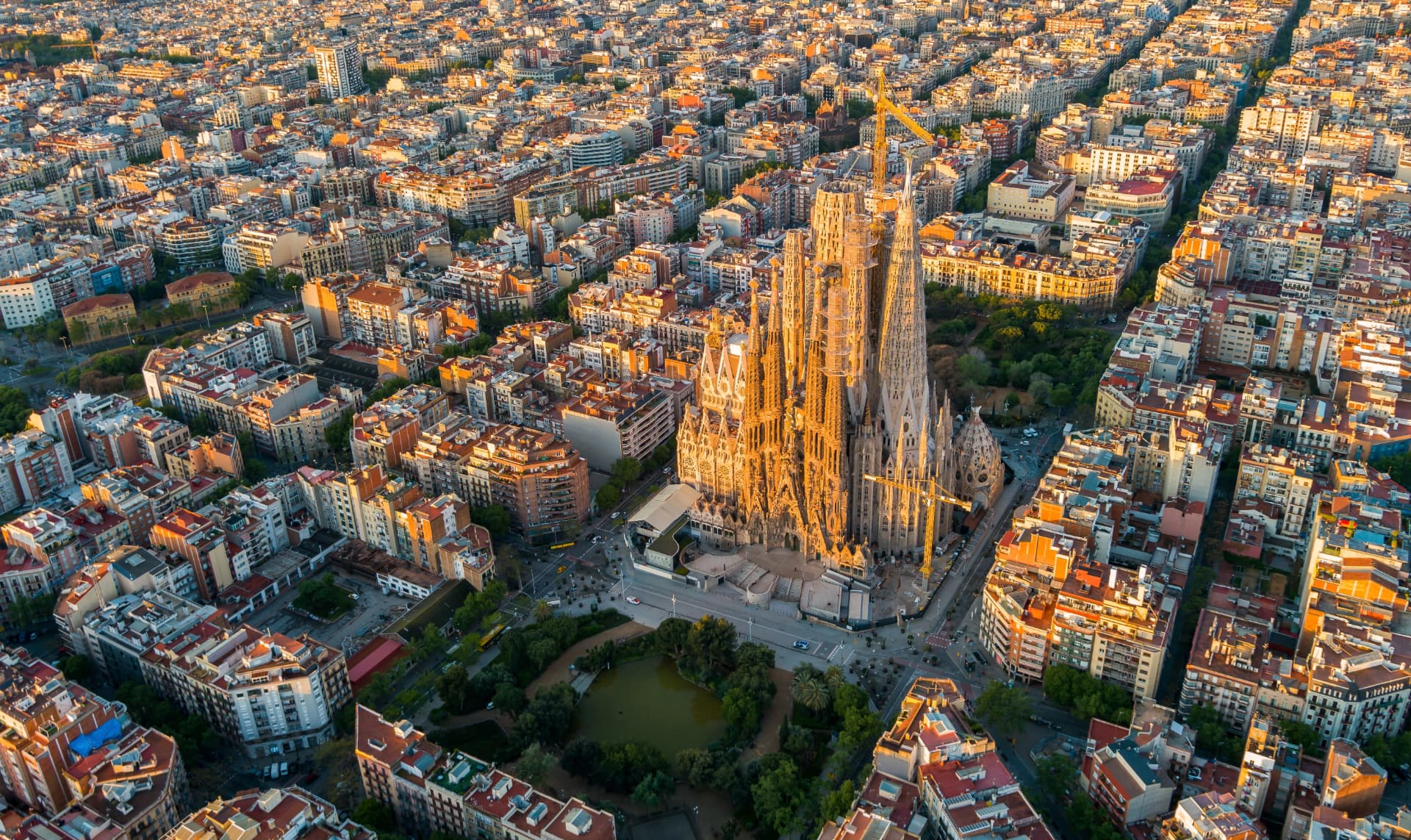 The Sagrada Família basilica rising above the Eixample grid of Barcelona at golden hour, seen from above