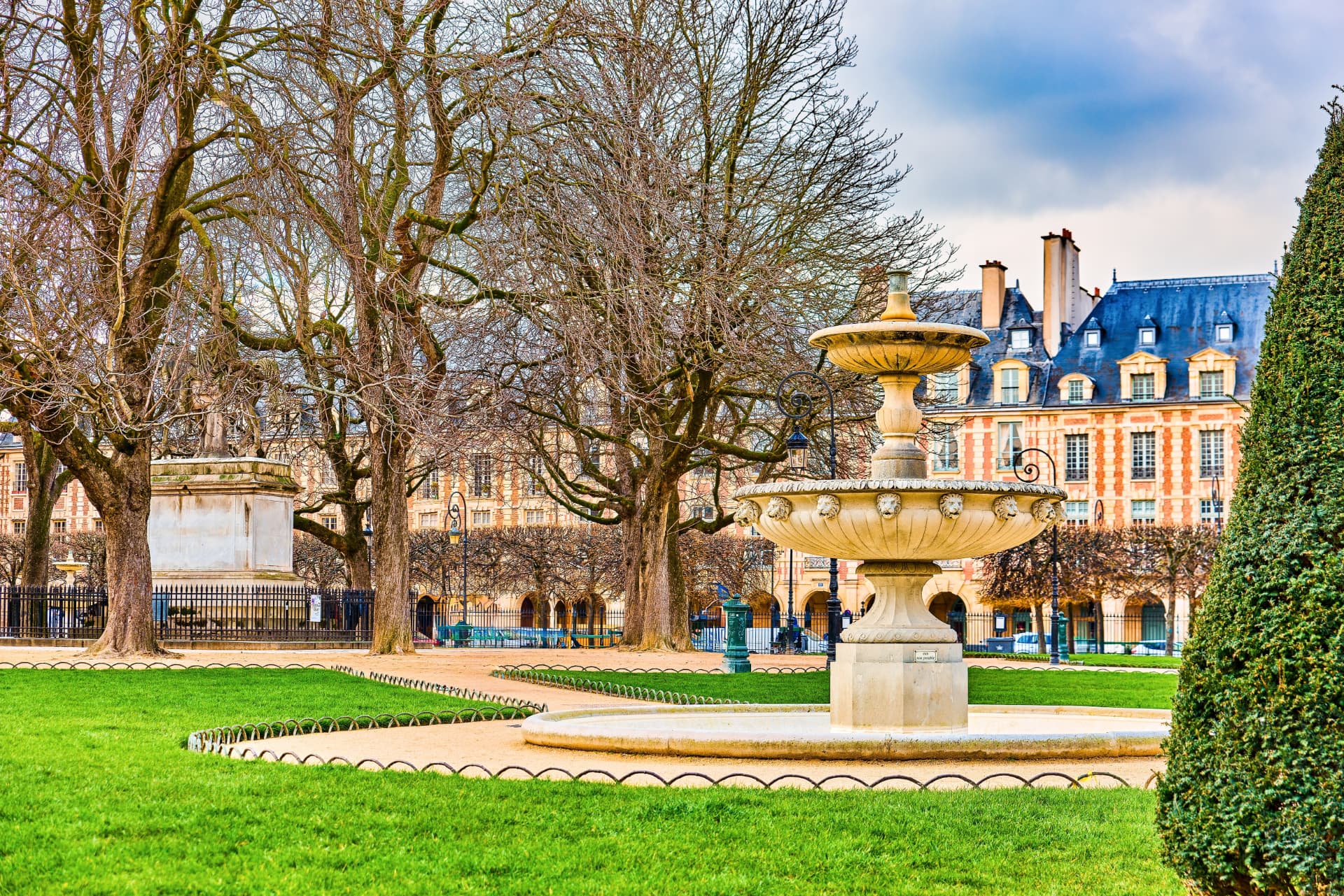 The ornamental fountain and lion statue of the Place des Vosges in early spring, with bare trees and manicured hedges