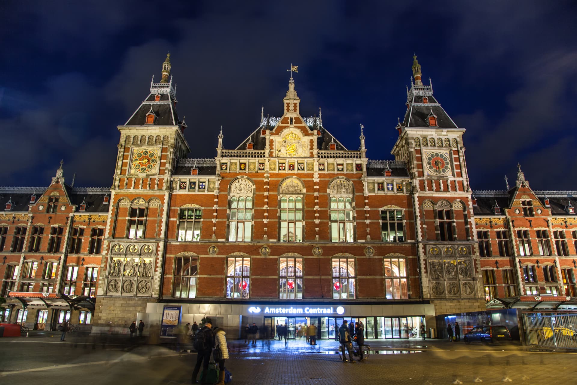 Front façade of Amsterdam Centraal Station illuminated at night with its two clock towers