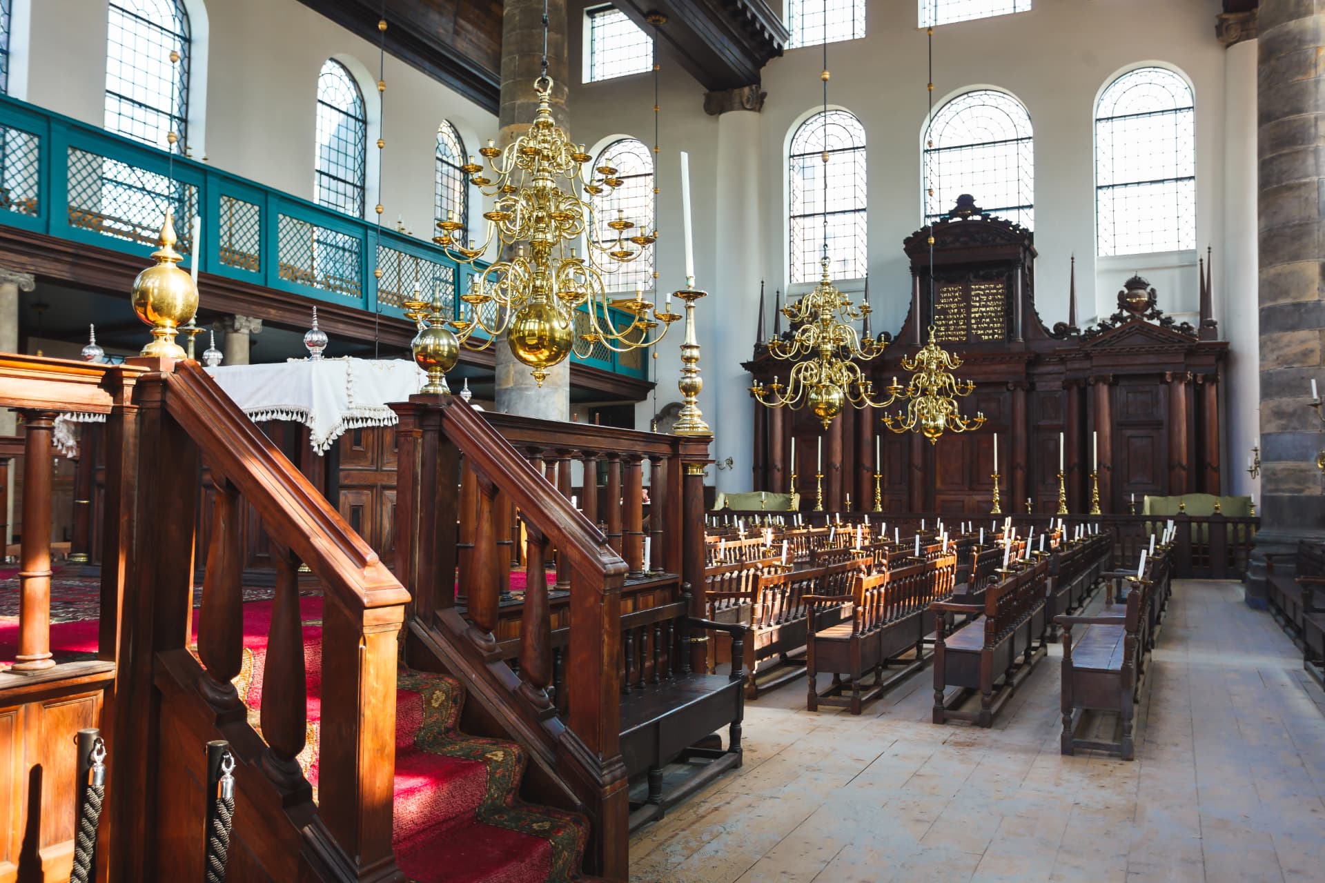 The bimah and ark of the Portuguese Synagogue in Amsterdam with red-carpeted steps, brass chandeliers and the women's gallery