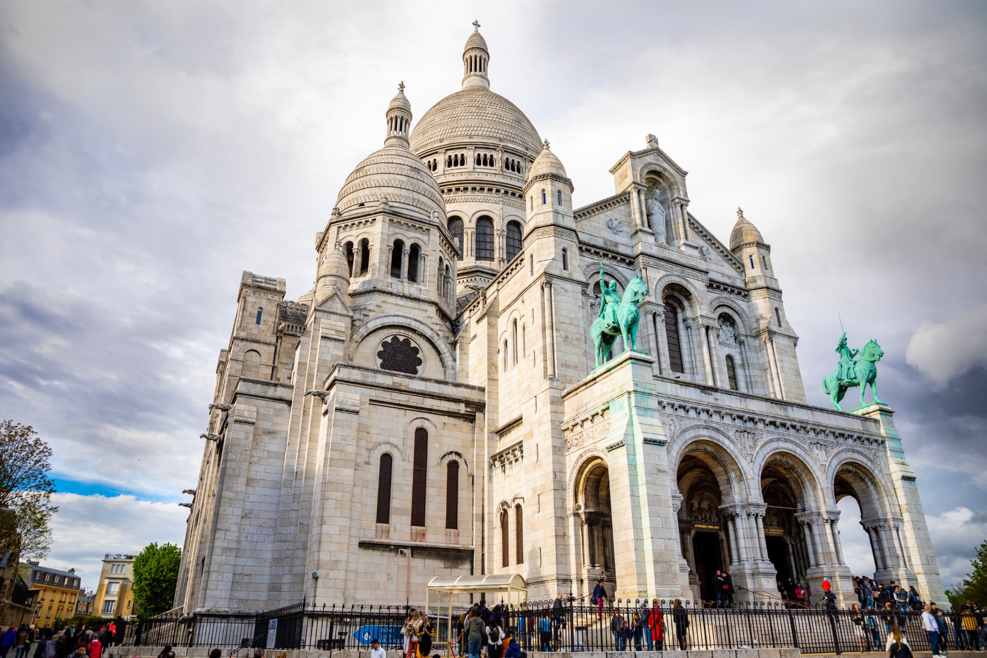 The white stone façade and domes of Sacré-Cœur Basilica in Montmartre, with two bronze equestrian statues above the entrance arches