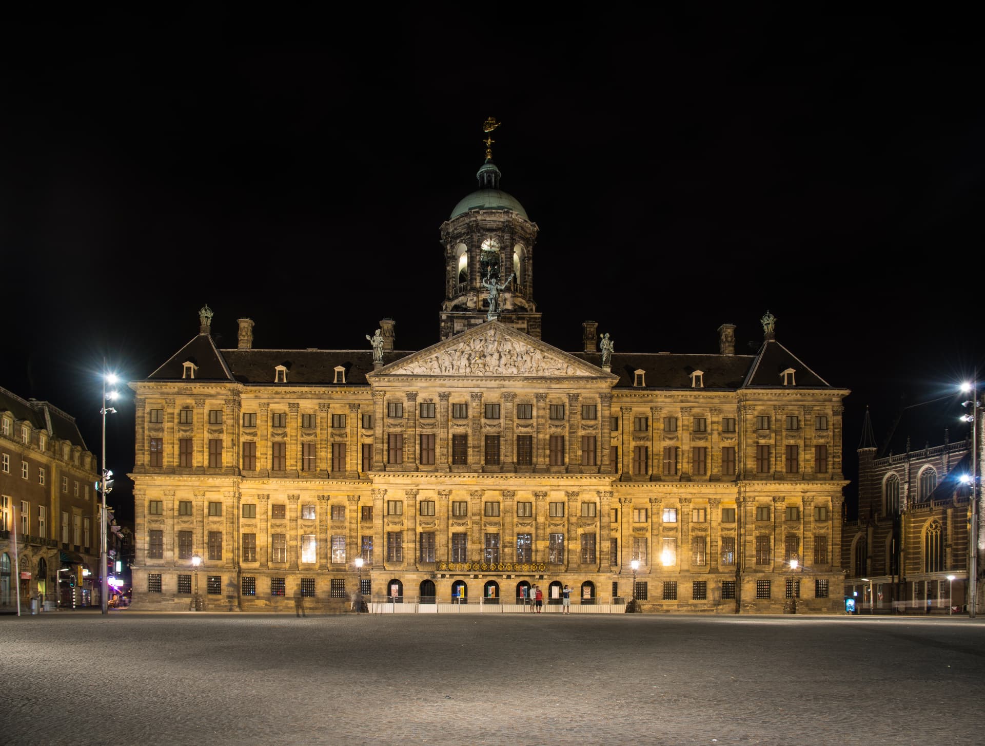 The Royal Palace of Amsterdam floodlit at night across an empty Dam Square