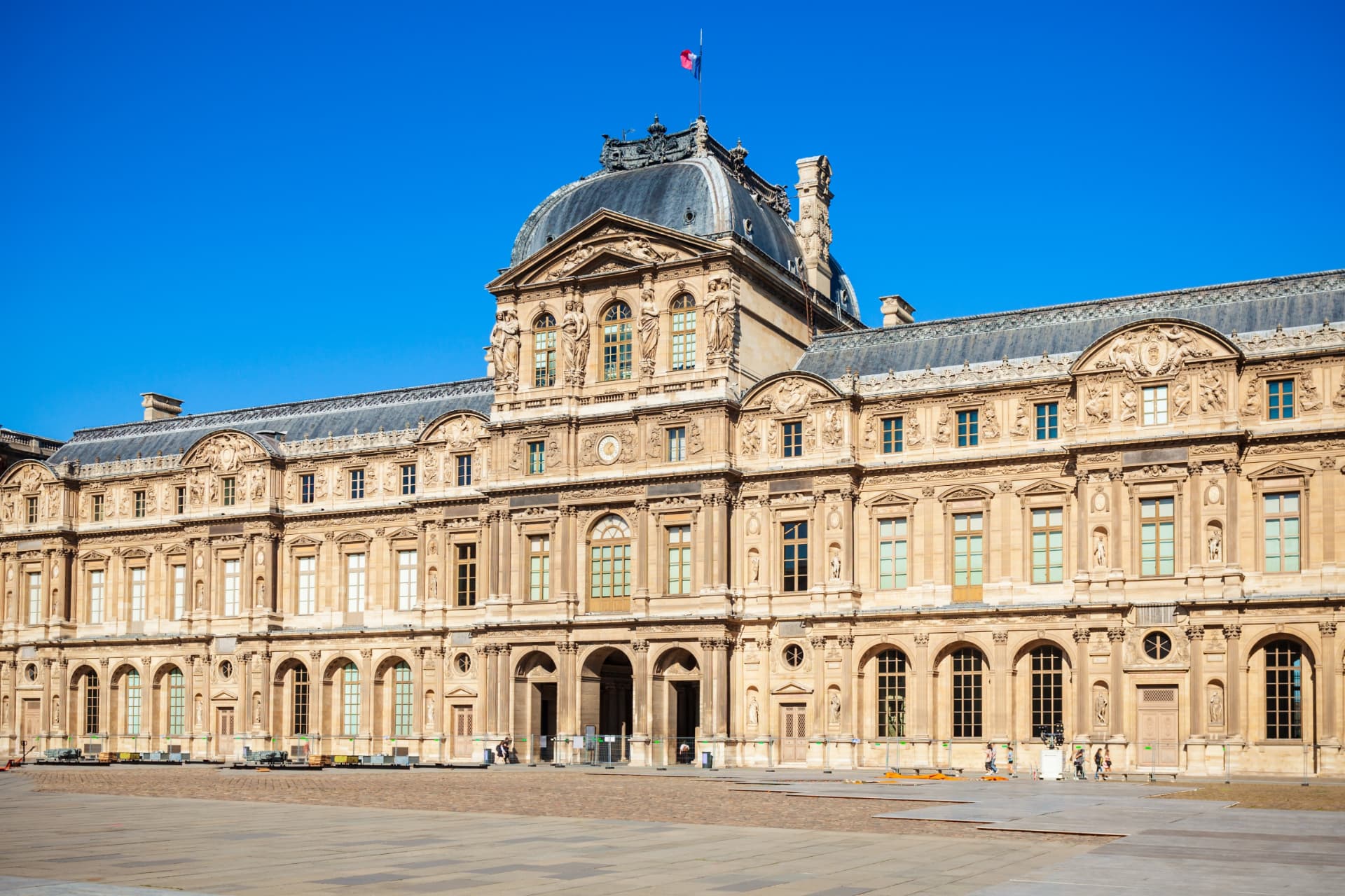 Stone façade of the Louvre palace in daylight with the French flag flying above