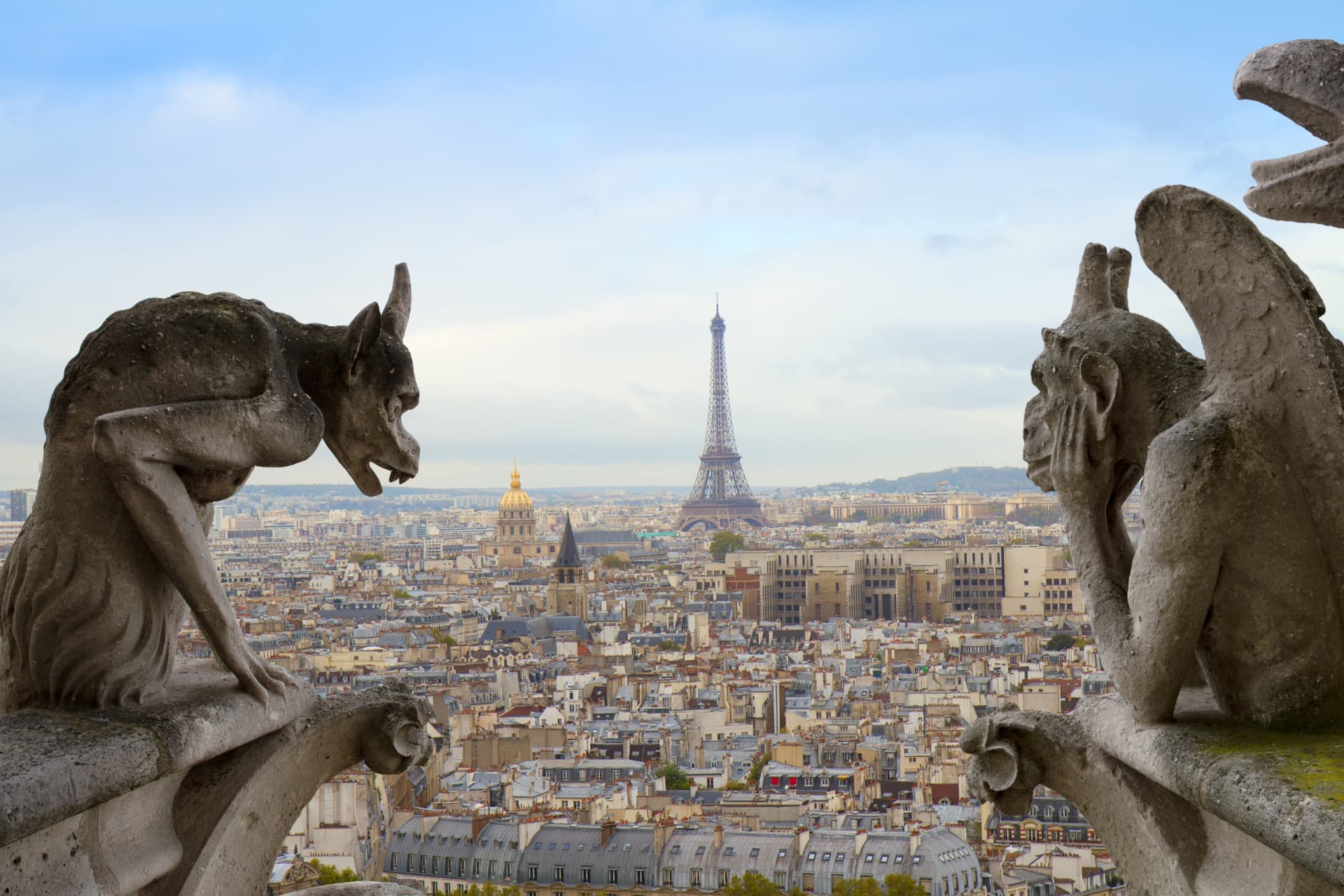 Stone gargoyles on the towers of Notre-Dame looking out over Paris with the Eiffel Tower in the distance