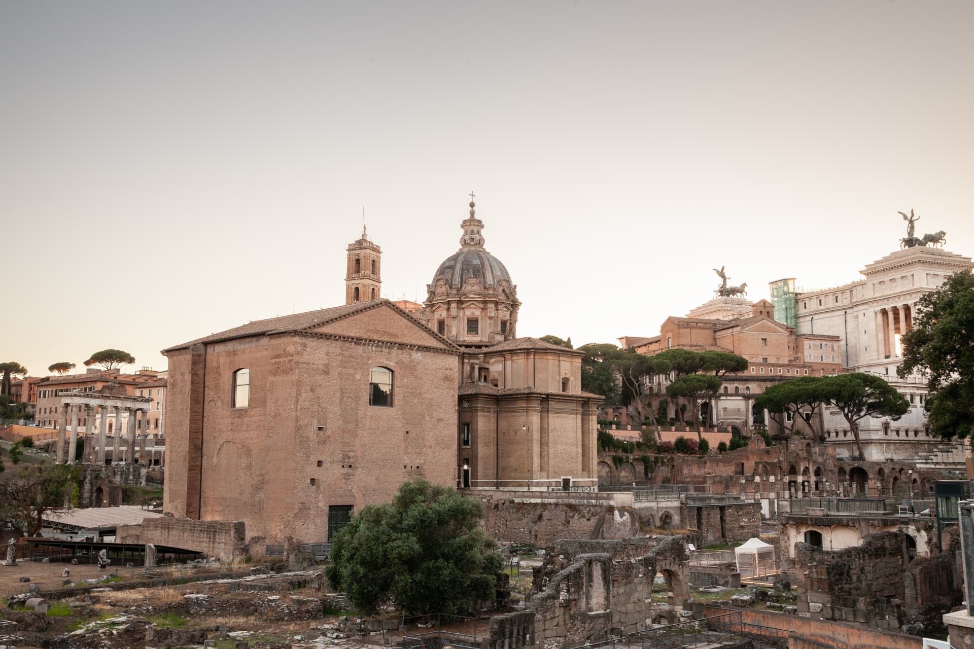 Curia Julia at dusk with a church dome and the Vittoriano behind it