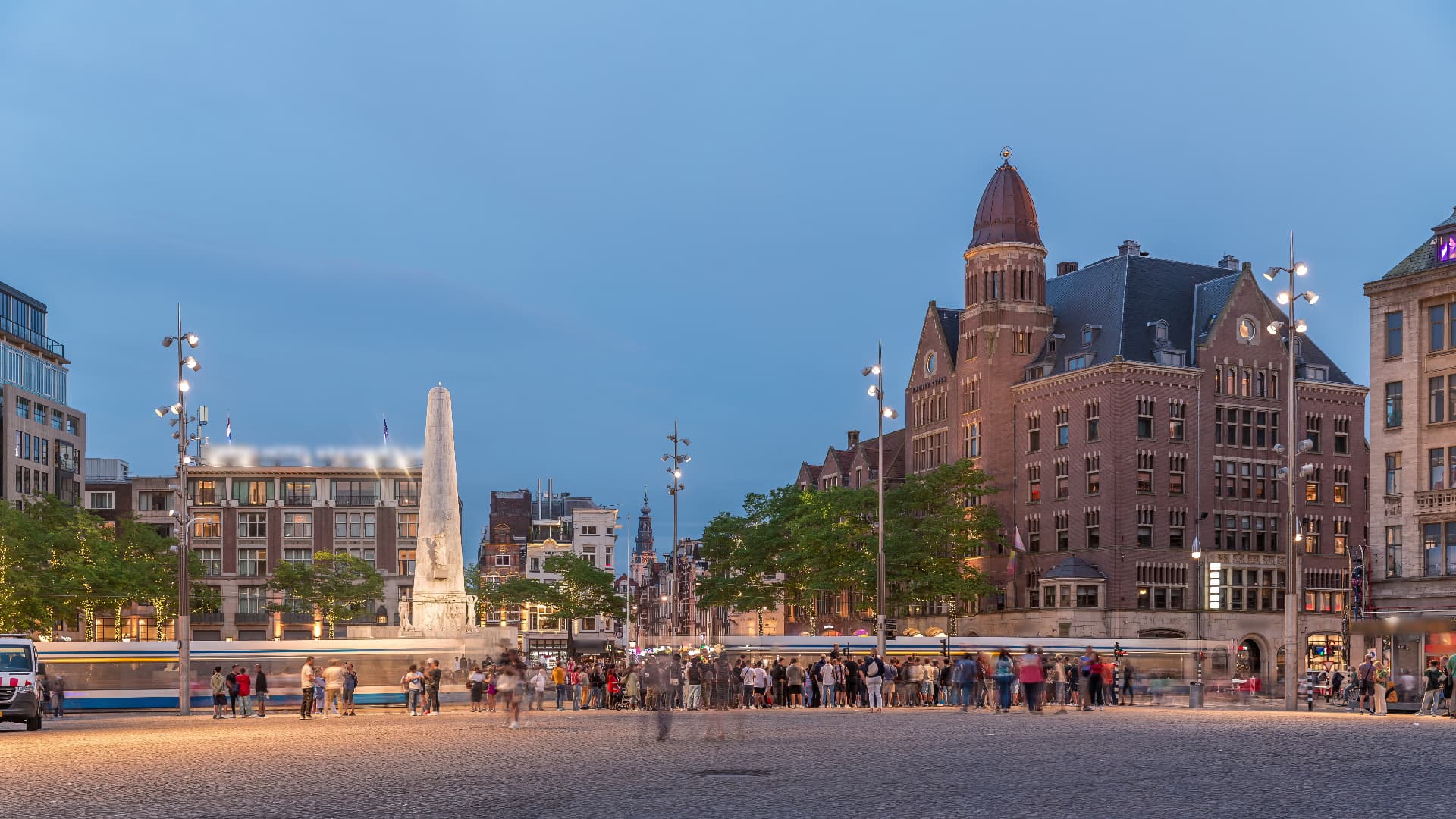 Dam Square in Amsterdam at dusk with a passing tram, the National Monument and historic buildings