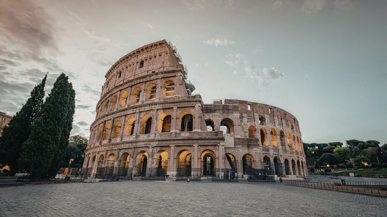 Colosseum at sunrise in Rome 2026 — warm morning light on travertine arches with Mediterranean cypress trees framing the ancient amphitheater