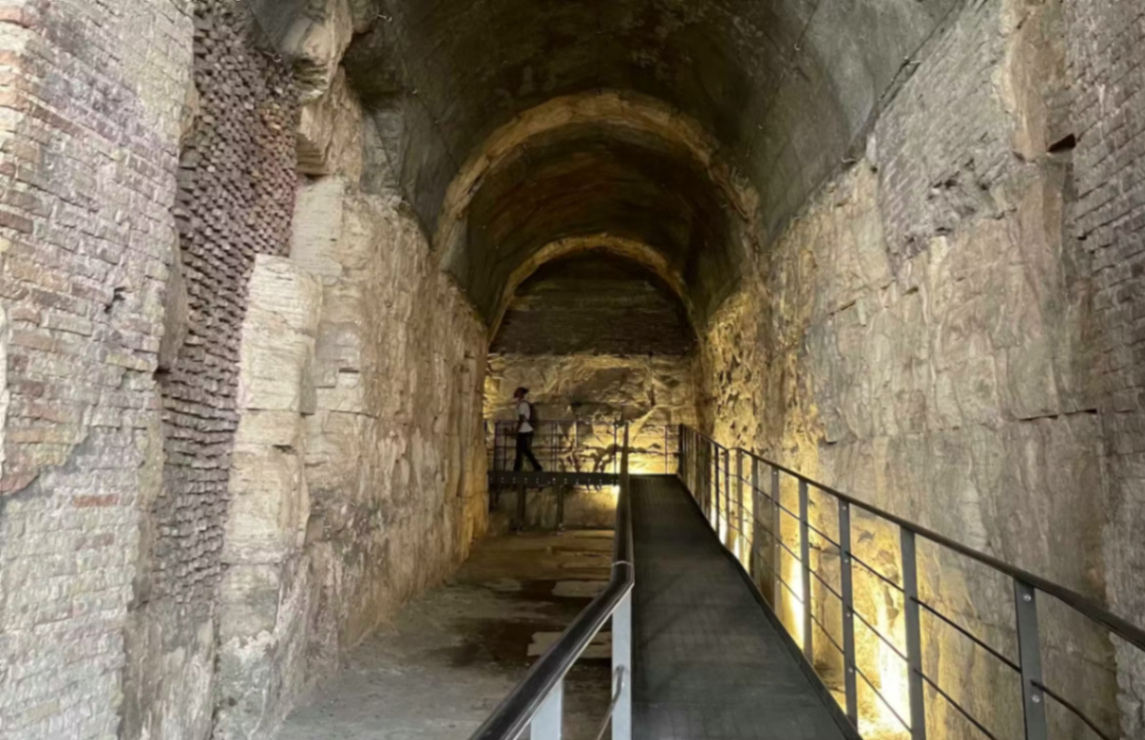 Dimly lit underground tunnel walkway inside the Colosseum hypogeum with ancient brick walls and metal railings