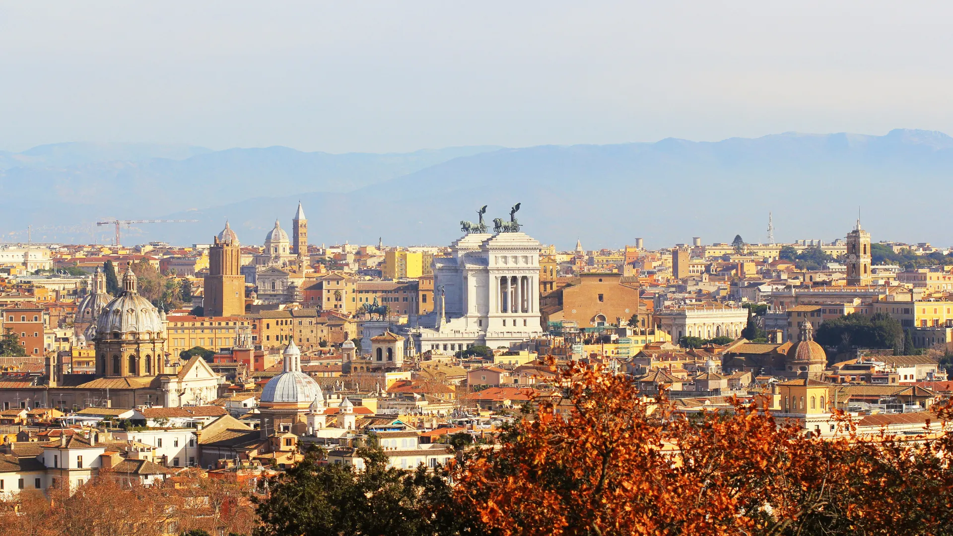 Sweeping panoramic view of Rome's historic skyline from Janiculum Hill terrace, showing St Peter's dome, terracotta rooftops, and the distant Alban Hills at golden hour