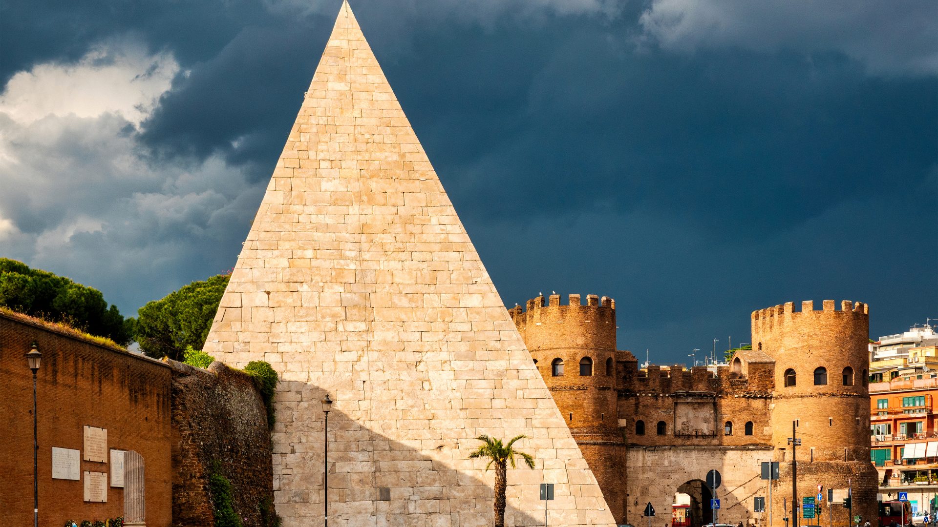 Pyramid of Cestius Rome 2026 — the 36-metre Carrara-marble ancient Roman pyramid built in 12 BC, glowing golden at sunset against the dark brick of the Aurelian Walls, with cypress trees of the Non-Catholic Cemetery to the right