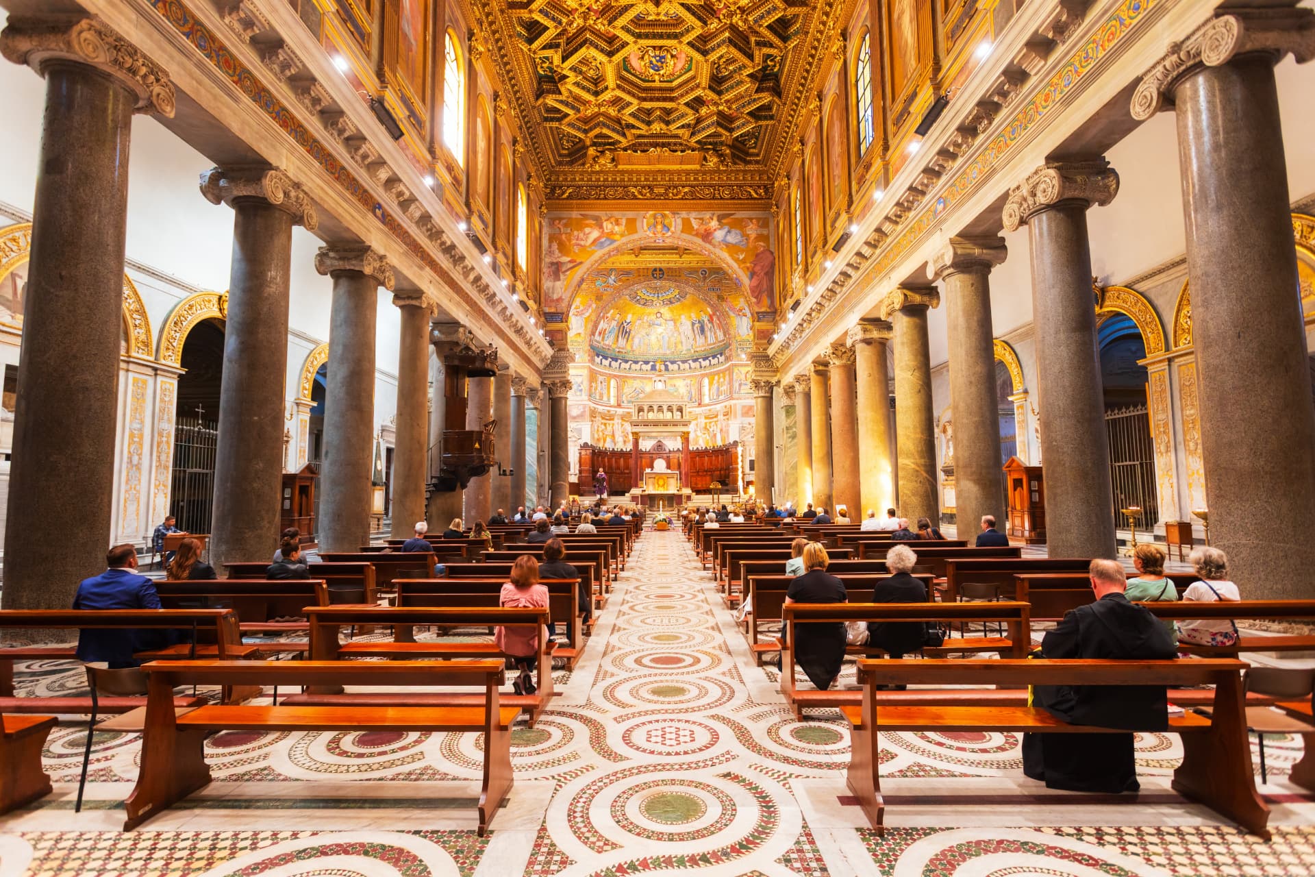Nave of the Basilica of Santa Maria in Trastevere with ancient granite columns, the gilded coffered ceiling and the golden apse mosaic above the altar