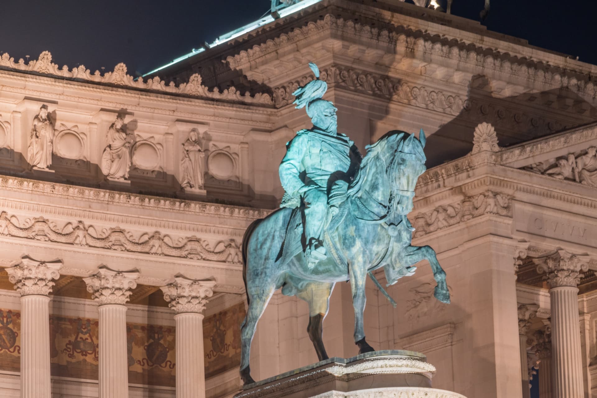 Illuminated bronze equestrian statue of King Victor Emmanuel II at night in front of the Vittoriano colonnade
