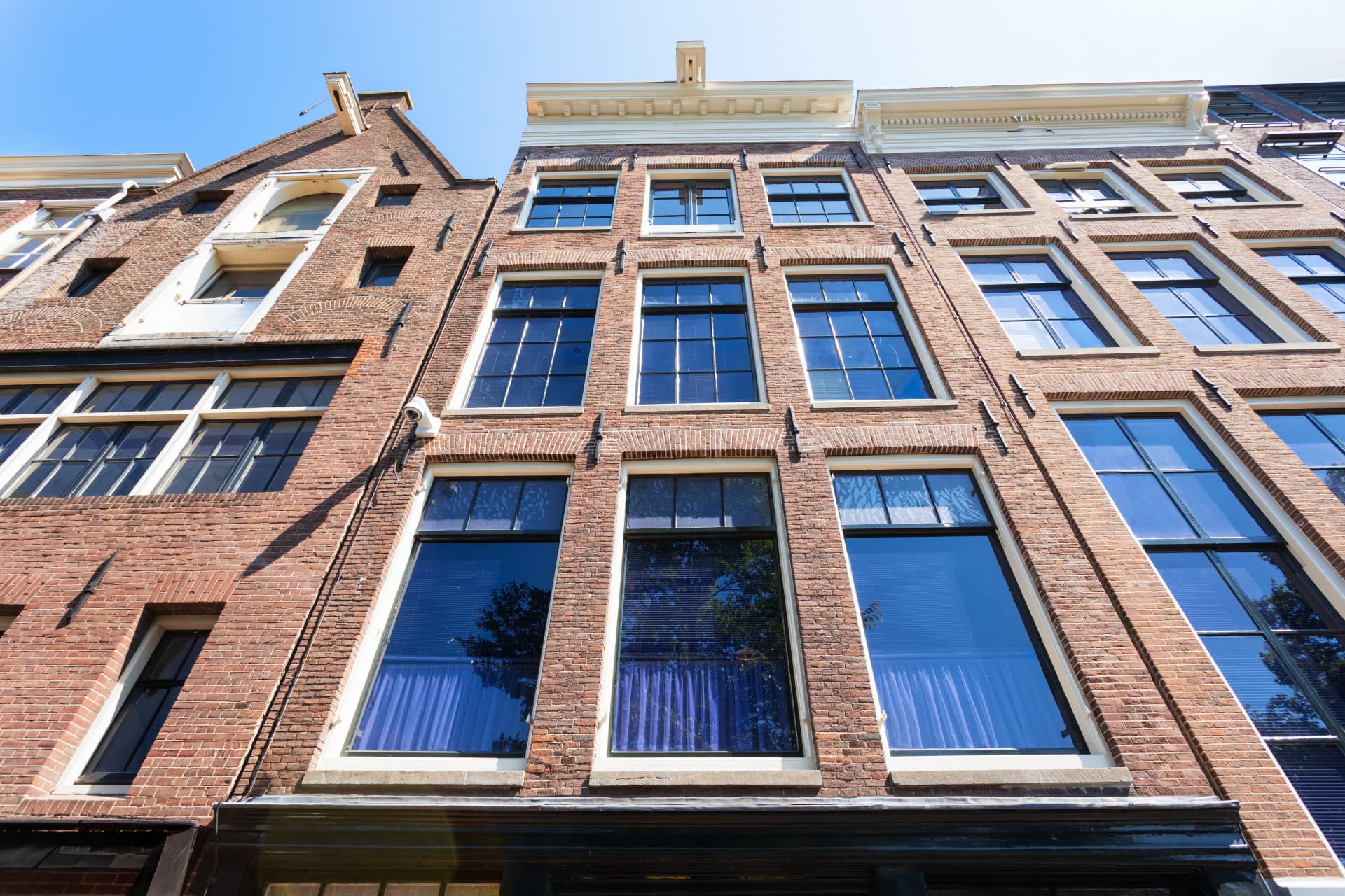 Traditional gabled brick canal houses along an Amsterdam canal under a clear blue sky