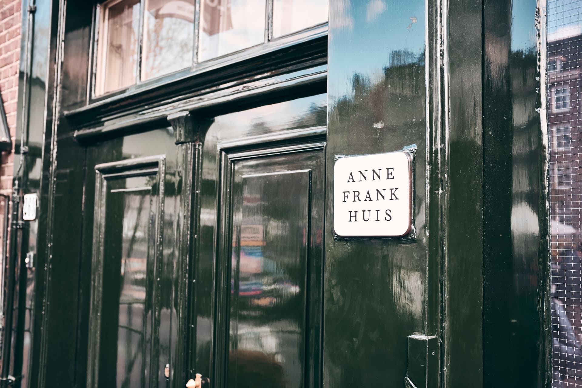 The dark doorway of the Anne Frank House at Prinsengracht 263 in Amsterdam, with the white Anne Frank Huis sign beside the door