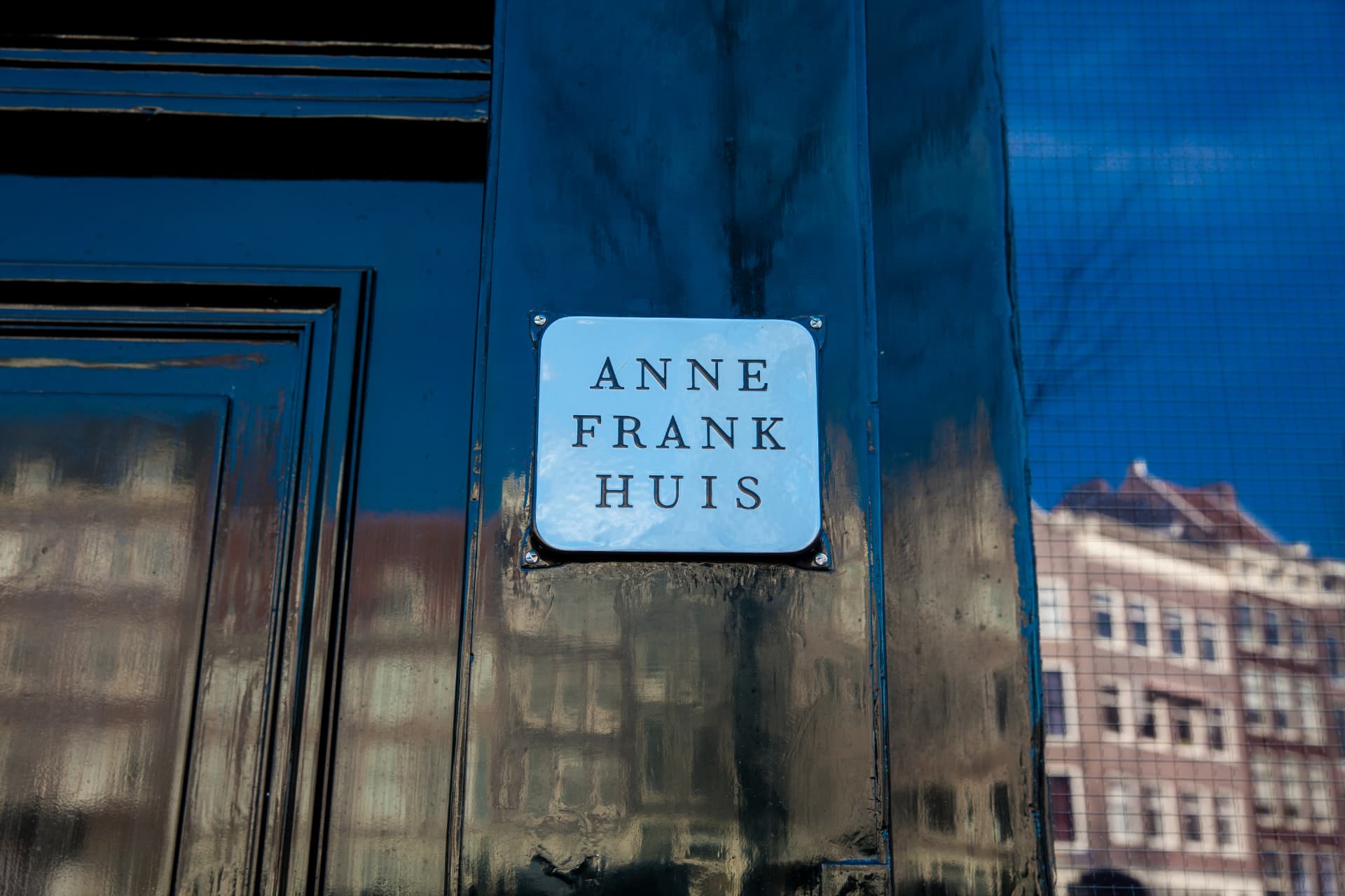 Close-up of the white Anne Frank Huis sign mounted on the dark painted wall beside the entrance door