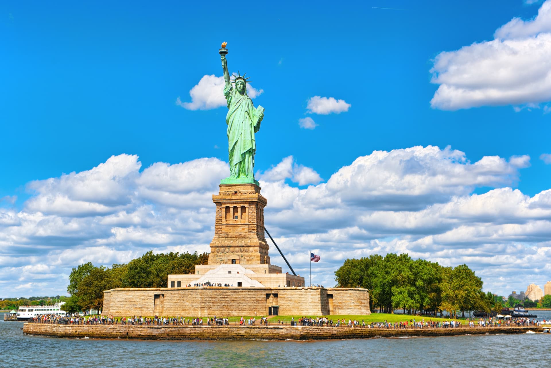 Liberty Island seen from the water, with the Statue of Liberty, the star-shaped Fort Wood base and the official ferry docked alongside