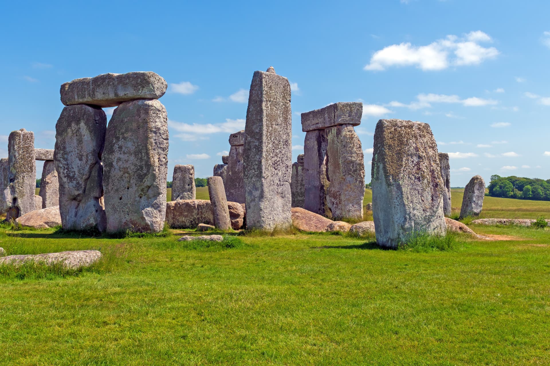 The sarsen stone circle and trilithons of Stonehenge on green grass under a bright blue sky